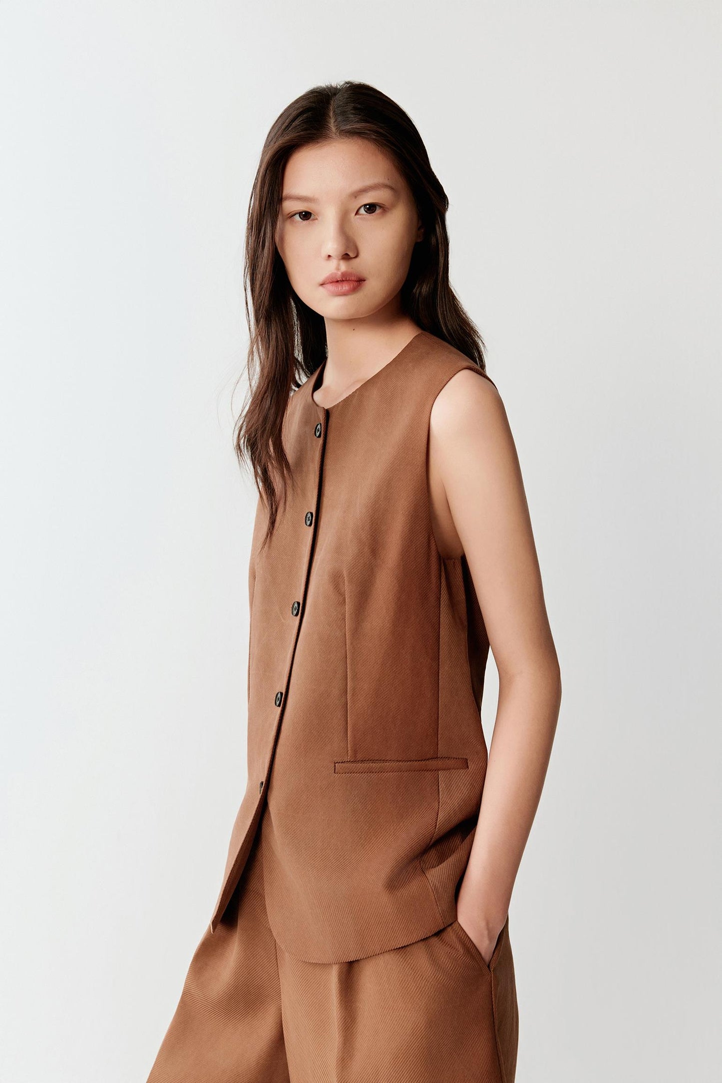 Close-up portrait focusing on the round neckline and front fastening, detailing the finely textured surface, tonal variation and structured woven appearance characteristic of the fabric