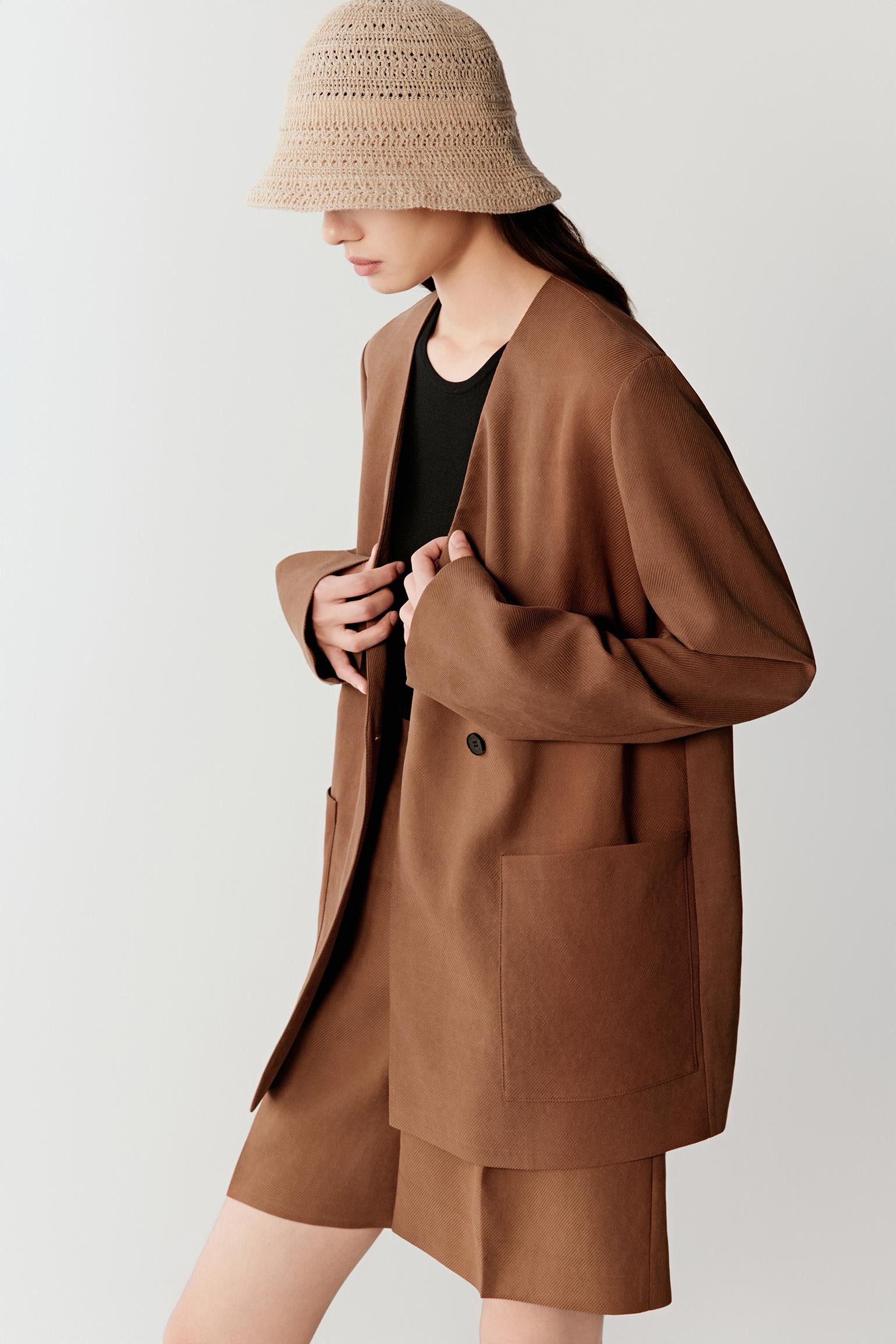 Close-up portrait focusing on the collarless neckline and front fastening, detailing the smooth matte texture, tonal depth and lightly textured woven surface of the warm brown fabric