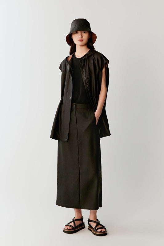 Full-length front view of a woman wearing a deep black sleeveless Gambiered Canton Gauze jacket with a fluid elongated silhouette, highlighting the hooded construction, lightweight drape and softly structured matte surface