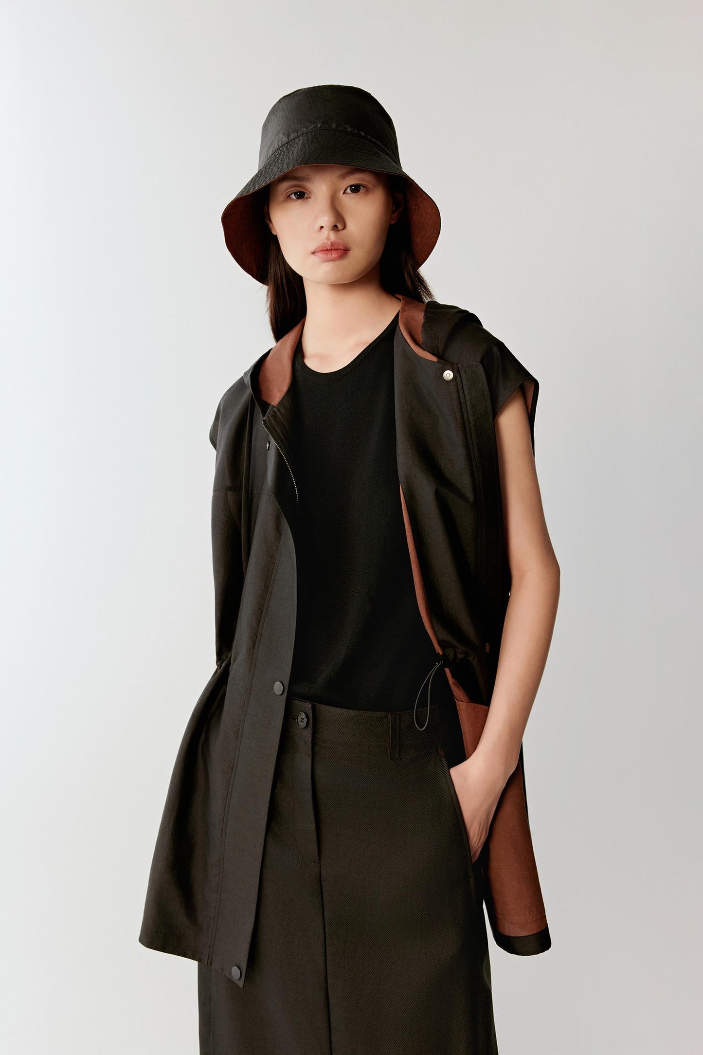 Close-up portrait focusing on the hood, neckline and upper body, detailing the smooth matte surface, subtle tonal depth and softly textured woven structure created through the dyeing process