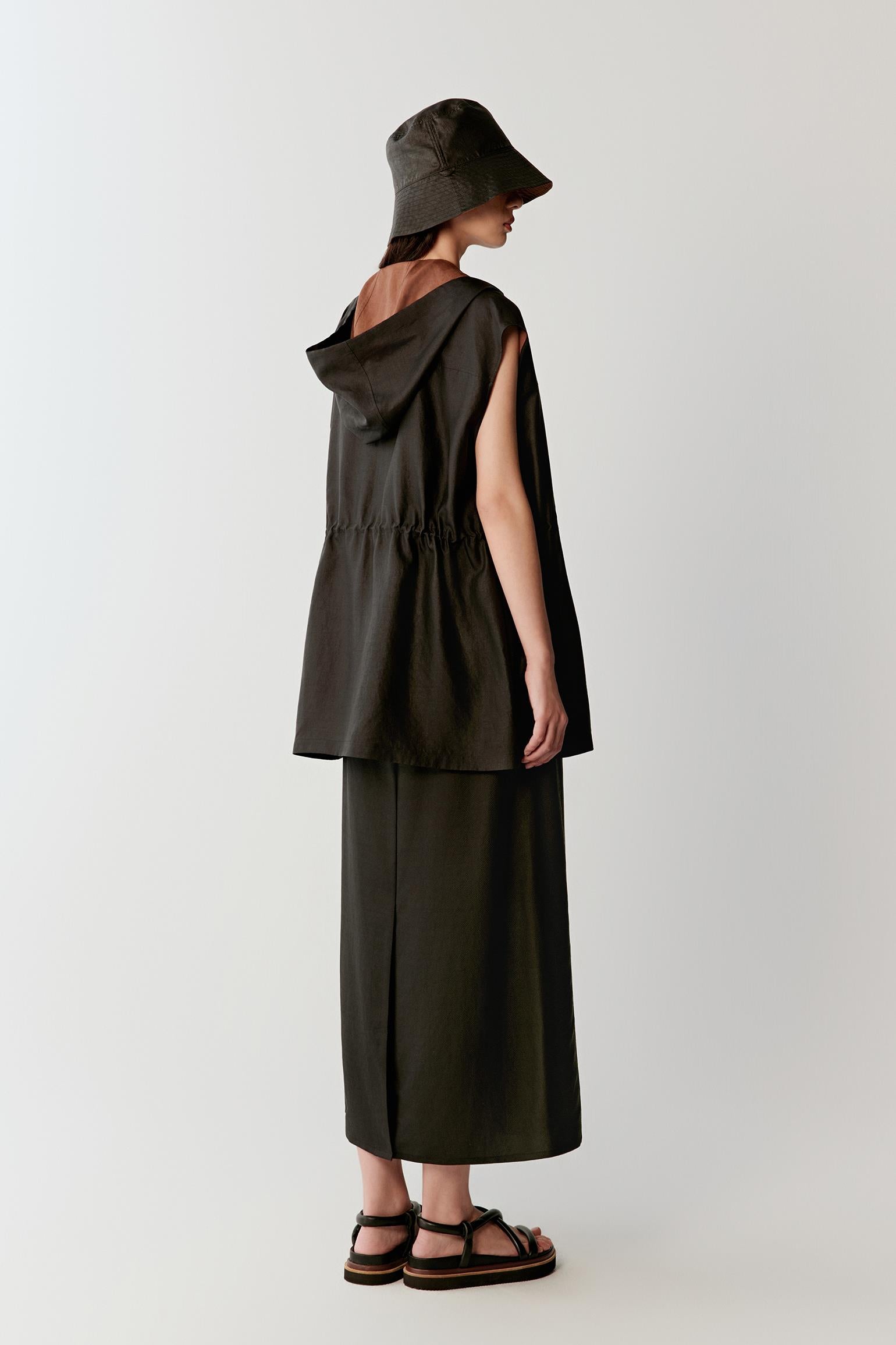 Full-length side or back view highlighting the elongated line, sleeveless construction and softly flowing drape of the deep black fabric as it moves around the body