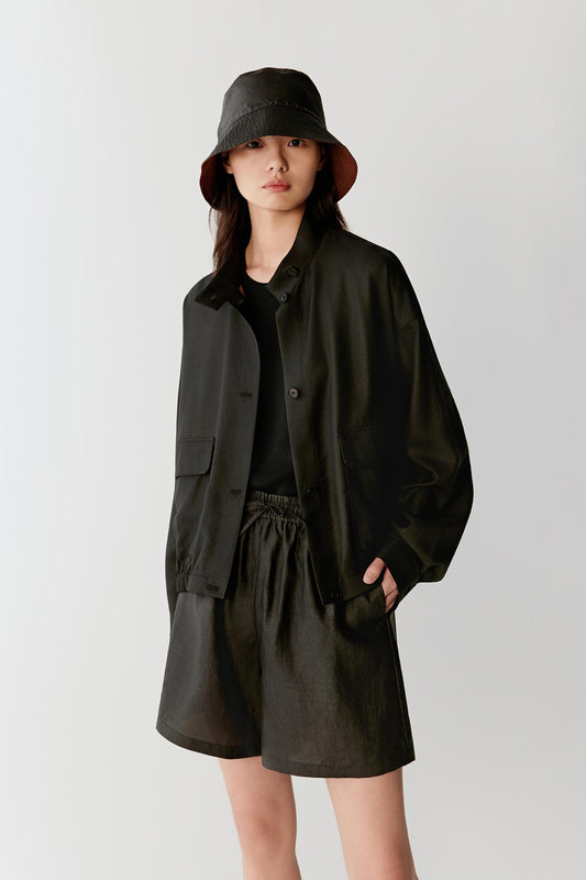 Front view of a woman wearing a black Gambiered Canton Gauze jacket with a softly structured silhouette, highlighting the compact woven texture, matte surface and tonal depth developed through the traditional dyeing process
