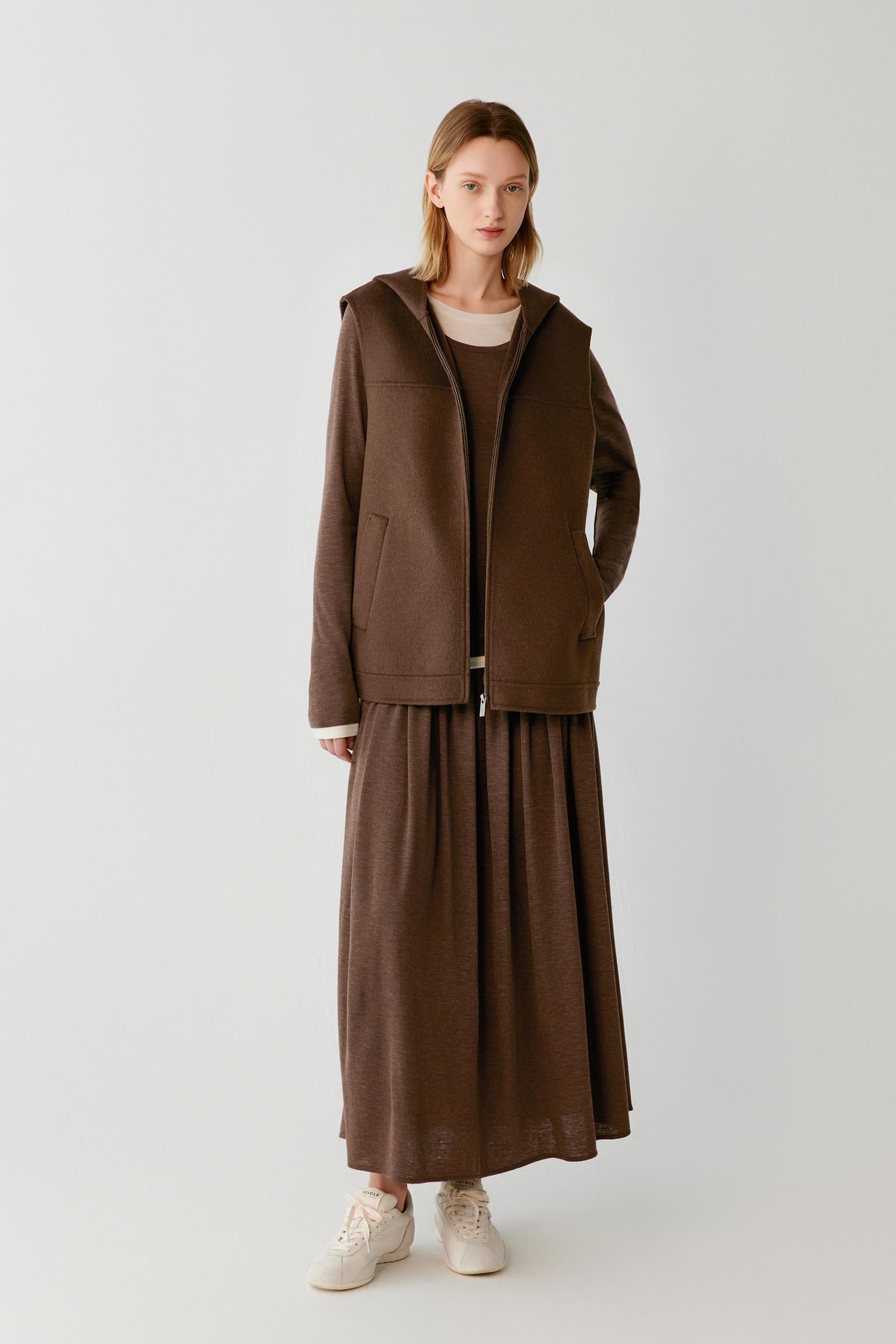 Woman wearing a brown hooded zip-up vest with a matching maxi skirt and white trainers.