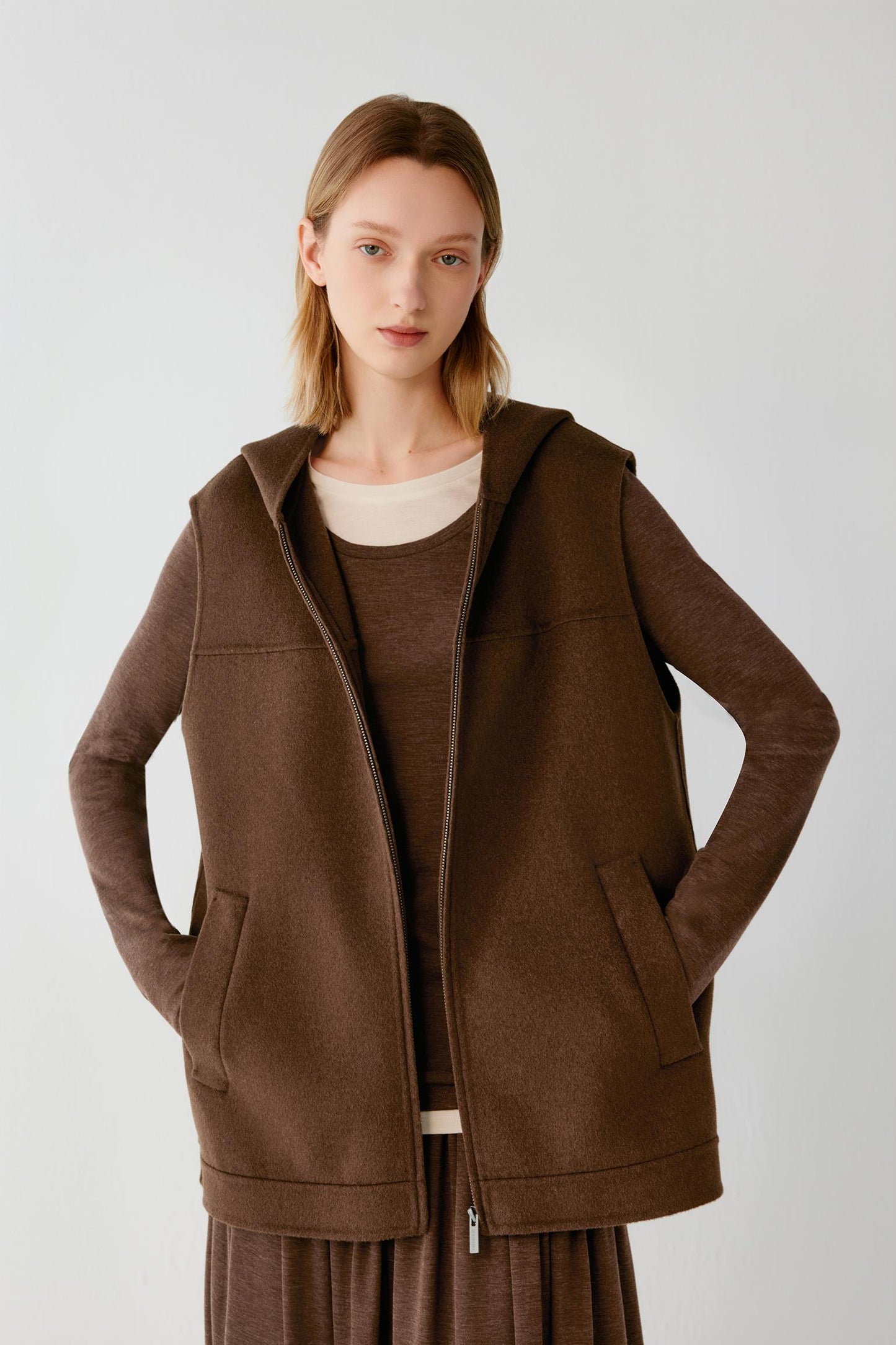 Woman wearing a brown hooded zip-up vest over a matching long-sleeve top.