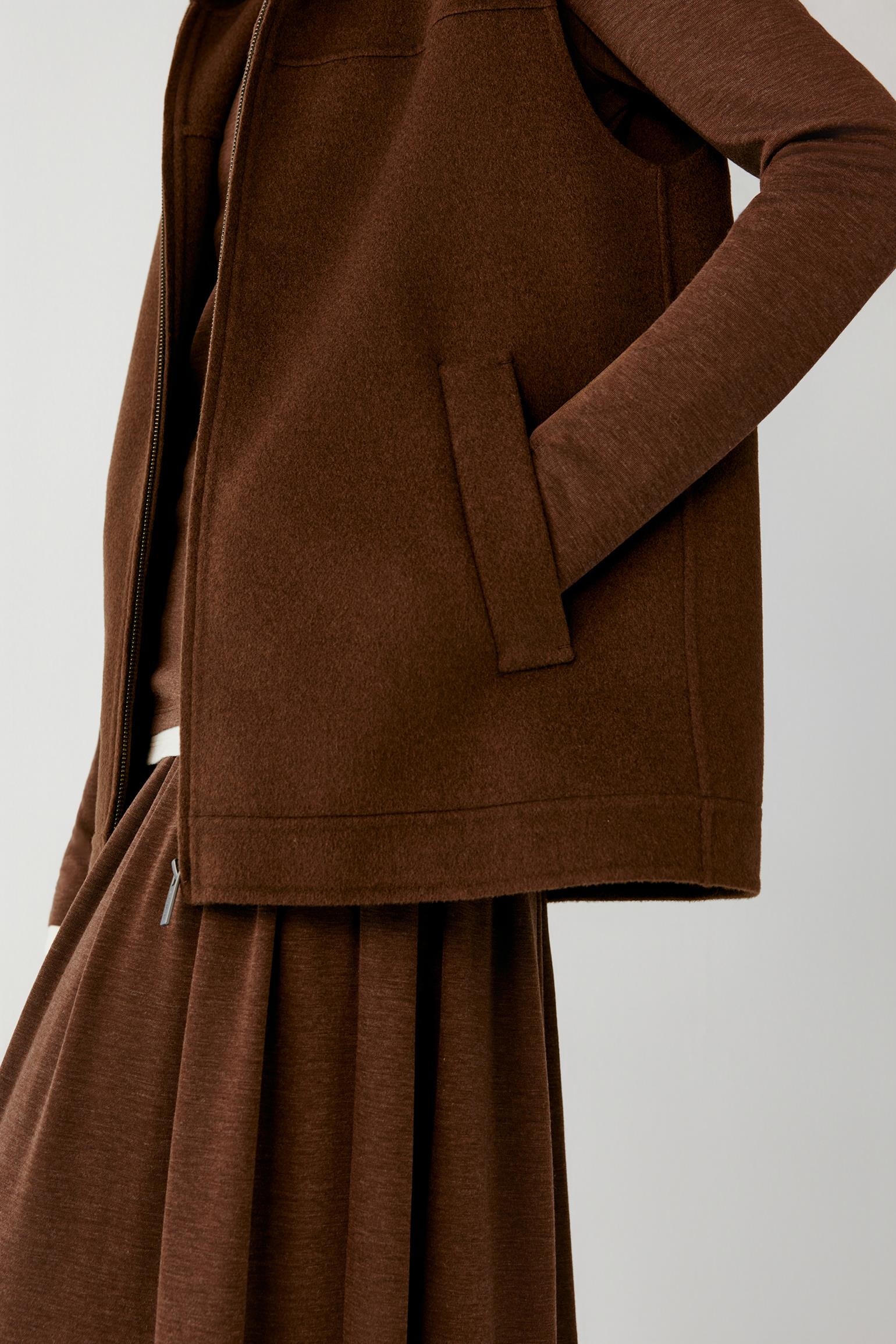 Close-up of the side pocket, zip fastening and textured fabric of a brown hooded vest.