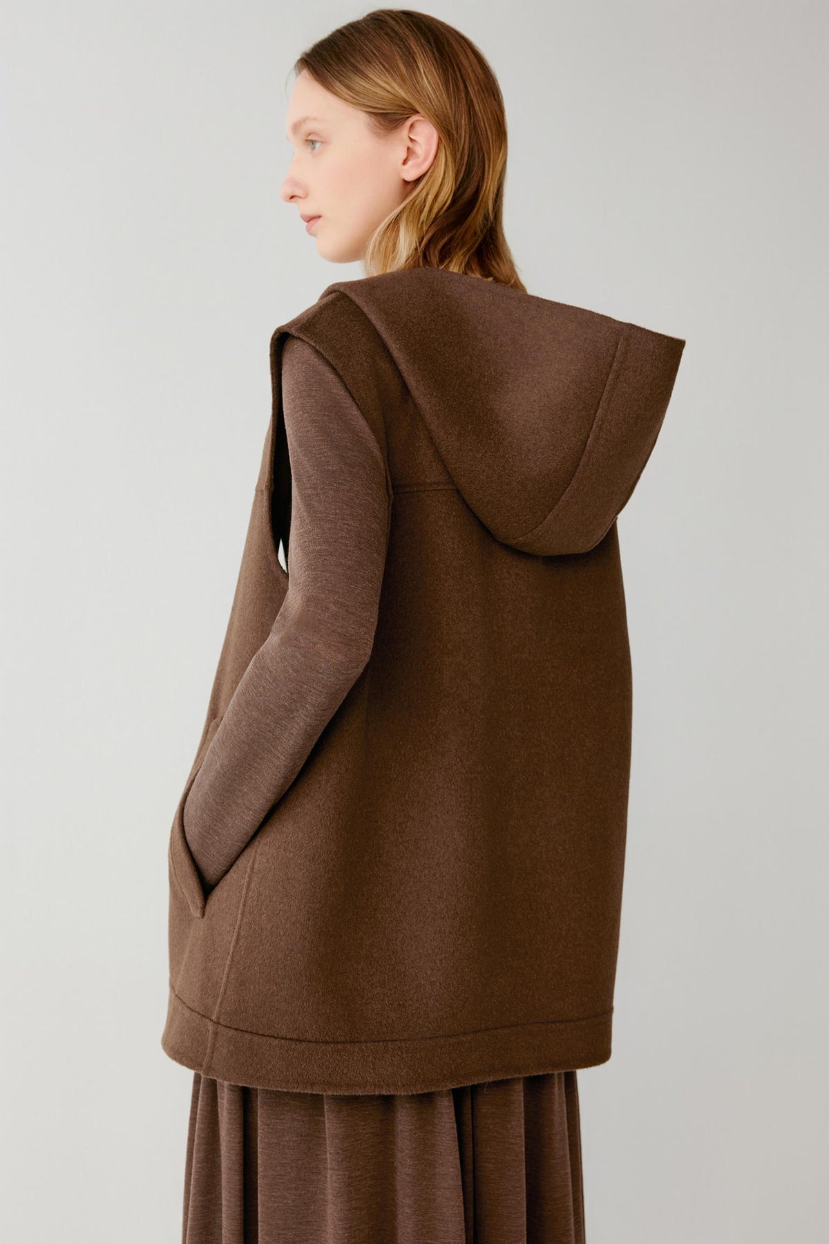 Back close-up of a woman wearing a brown hooded vest with side pockets.