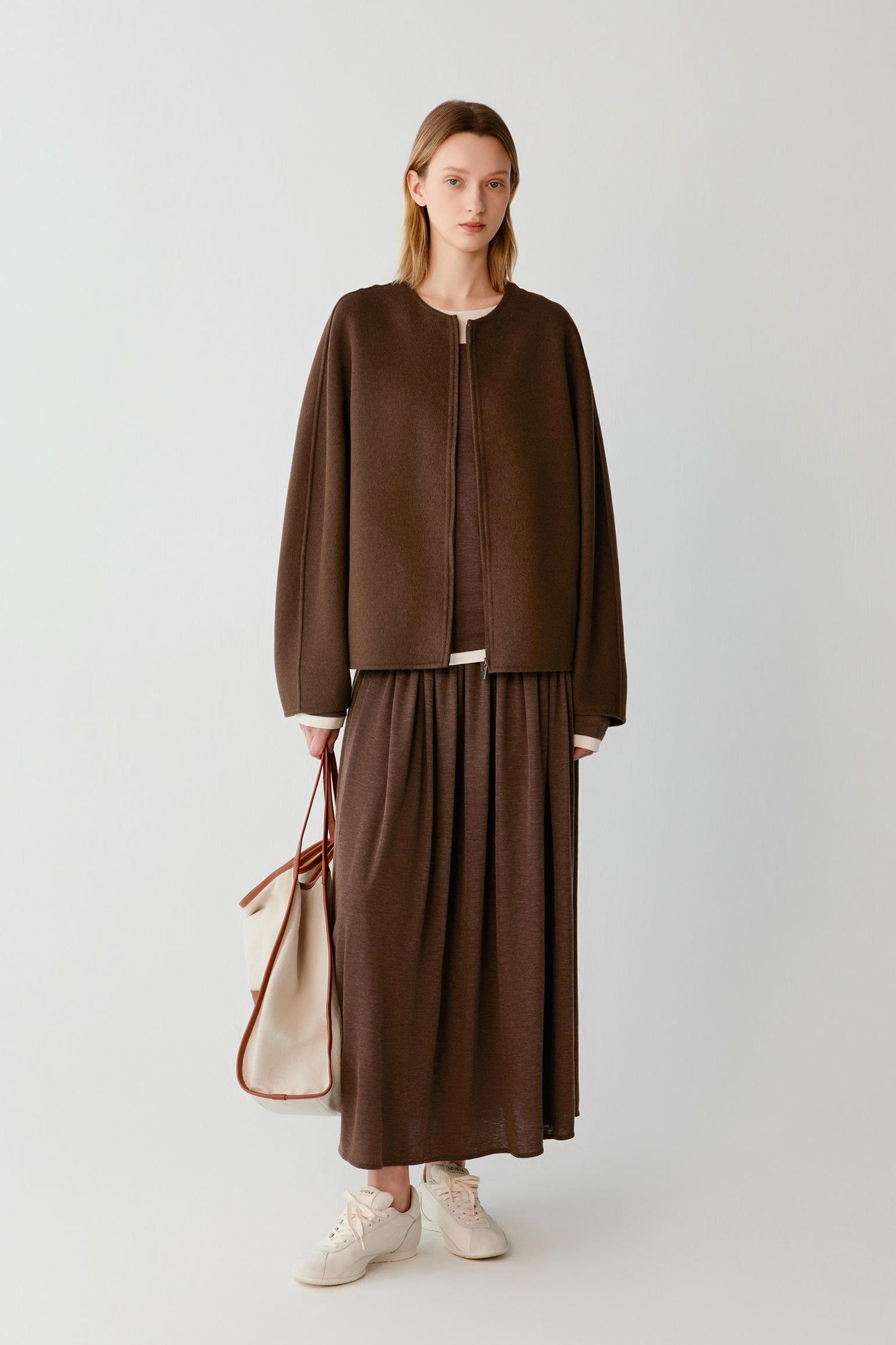 Woman wearing a brown zip-up jacket with a matching maxi skirt and white trainers.