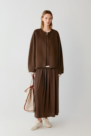 Woman wearing a brown zip-up jacket with a matching maxi skirt and white trainers.