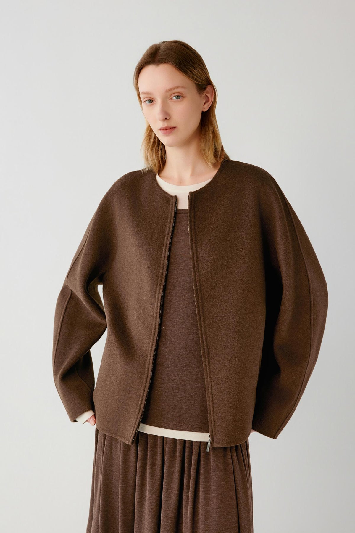 Woman wearing a brown collarless zip-up jacket over a matching top and skirt.