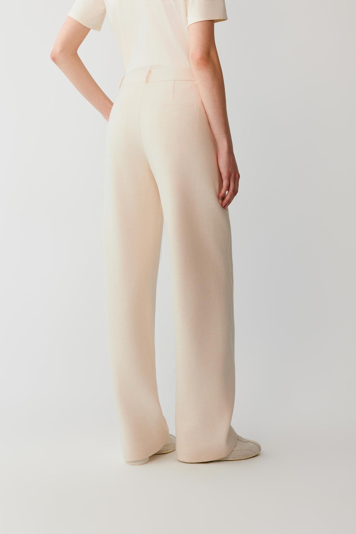 Side view of the beige cotton and yak trousers, showing the wide-leg silhouette and smooth interlock surface.