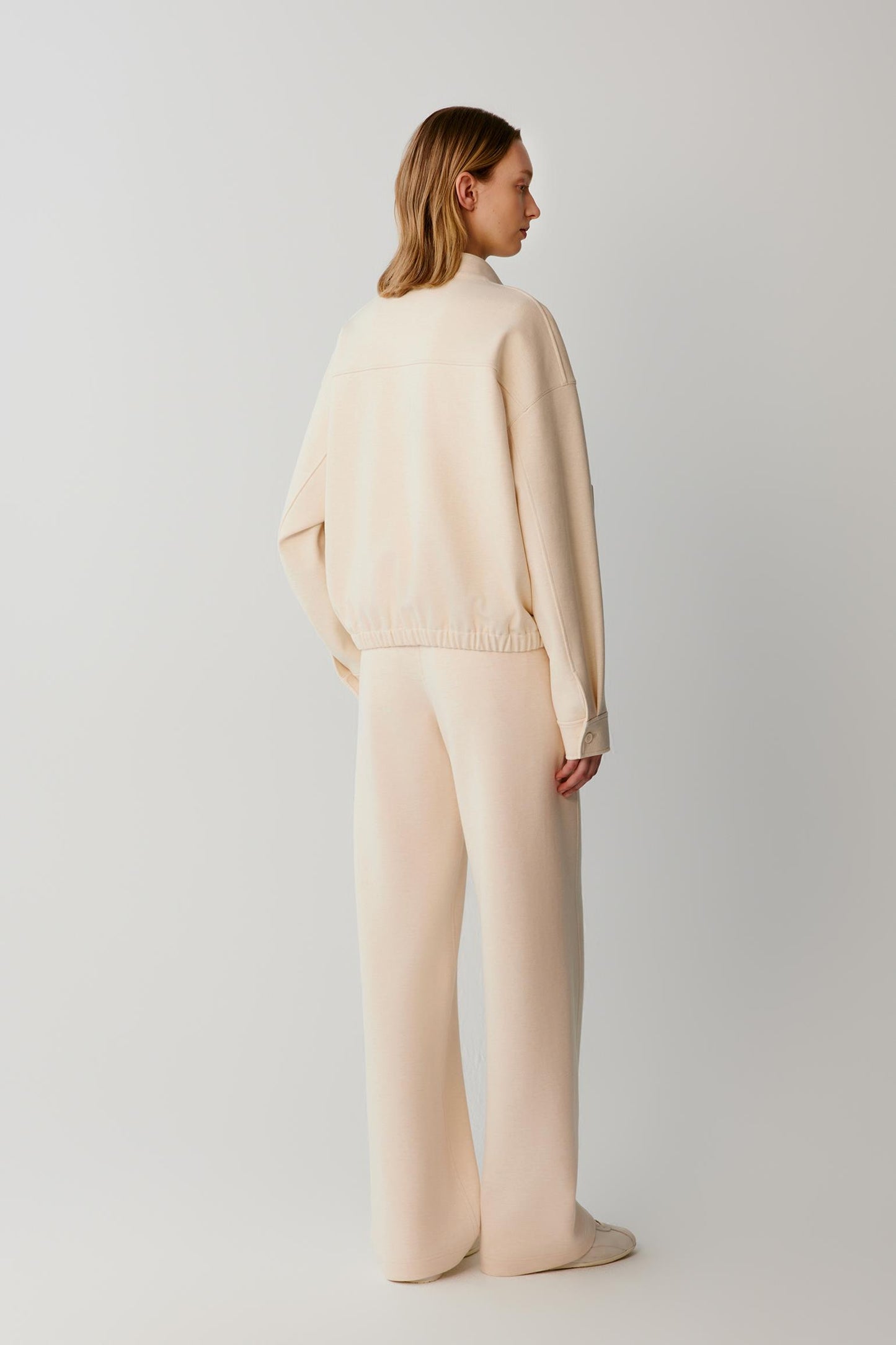 Back view of a woman wearing a cream jacket with matching wide-leg trousers.