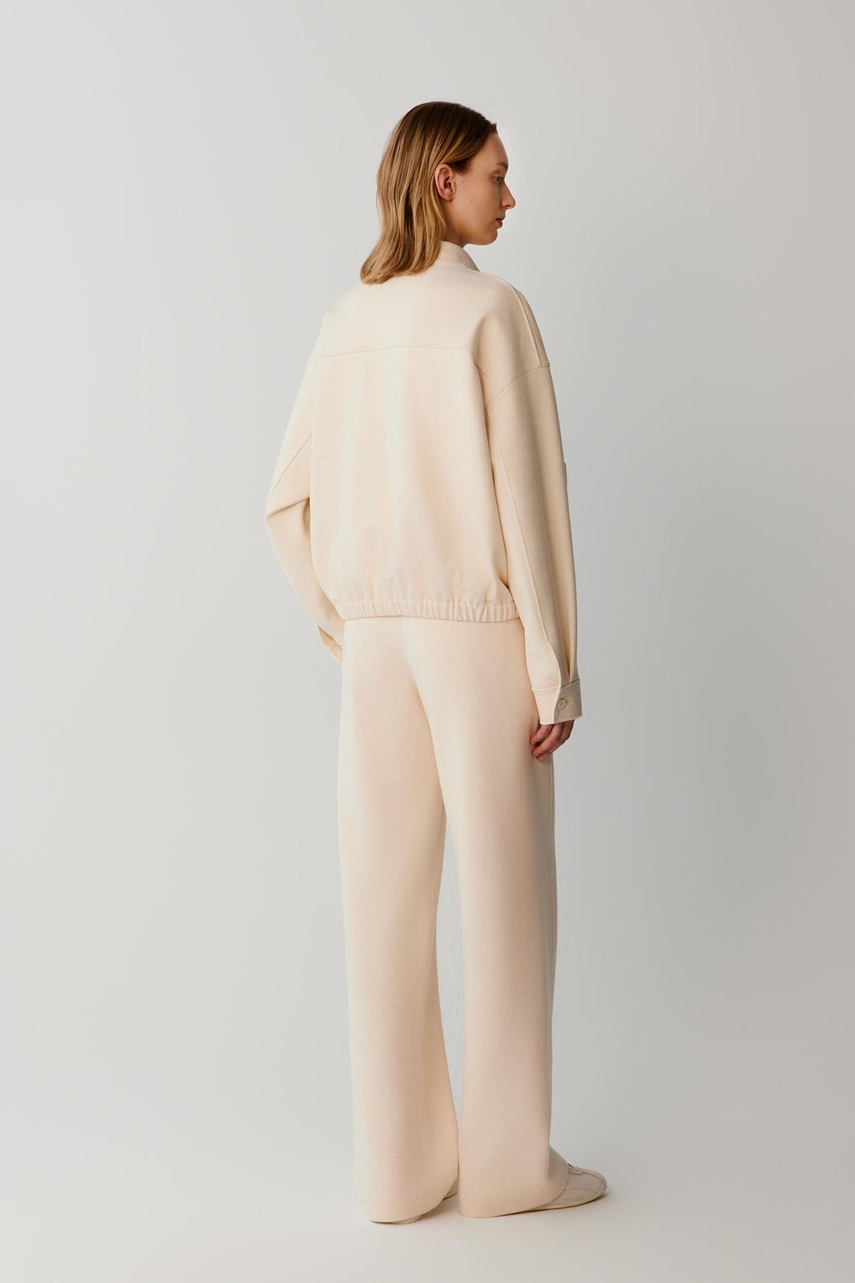 Back view of a woman wearing a cream jacket with matching wide-leg trousers.