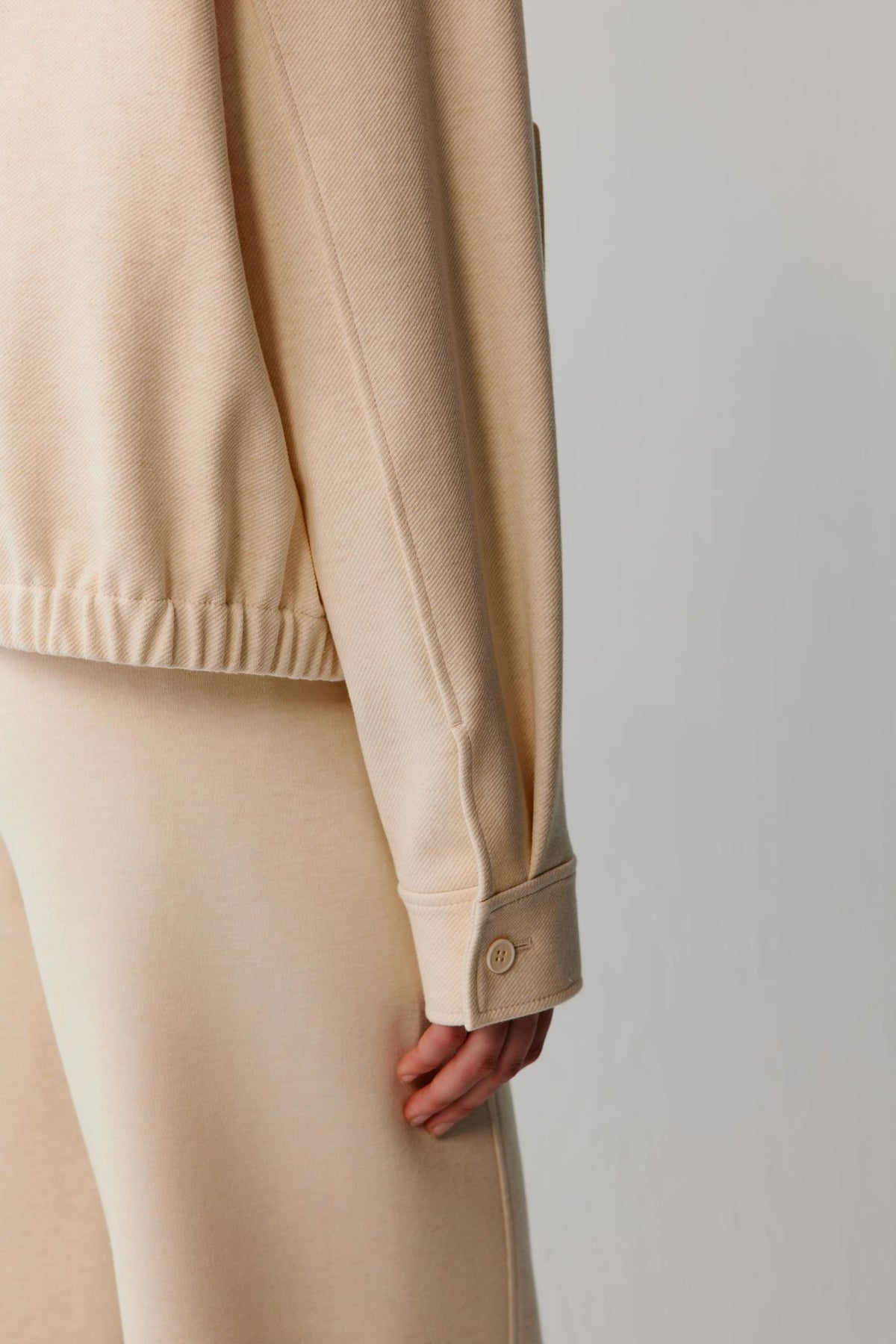 Close-up of the buttoned cuff, sleeve seam and elasticated hem of a cream jacket.