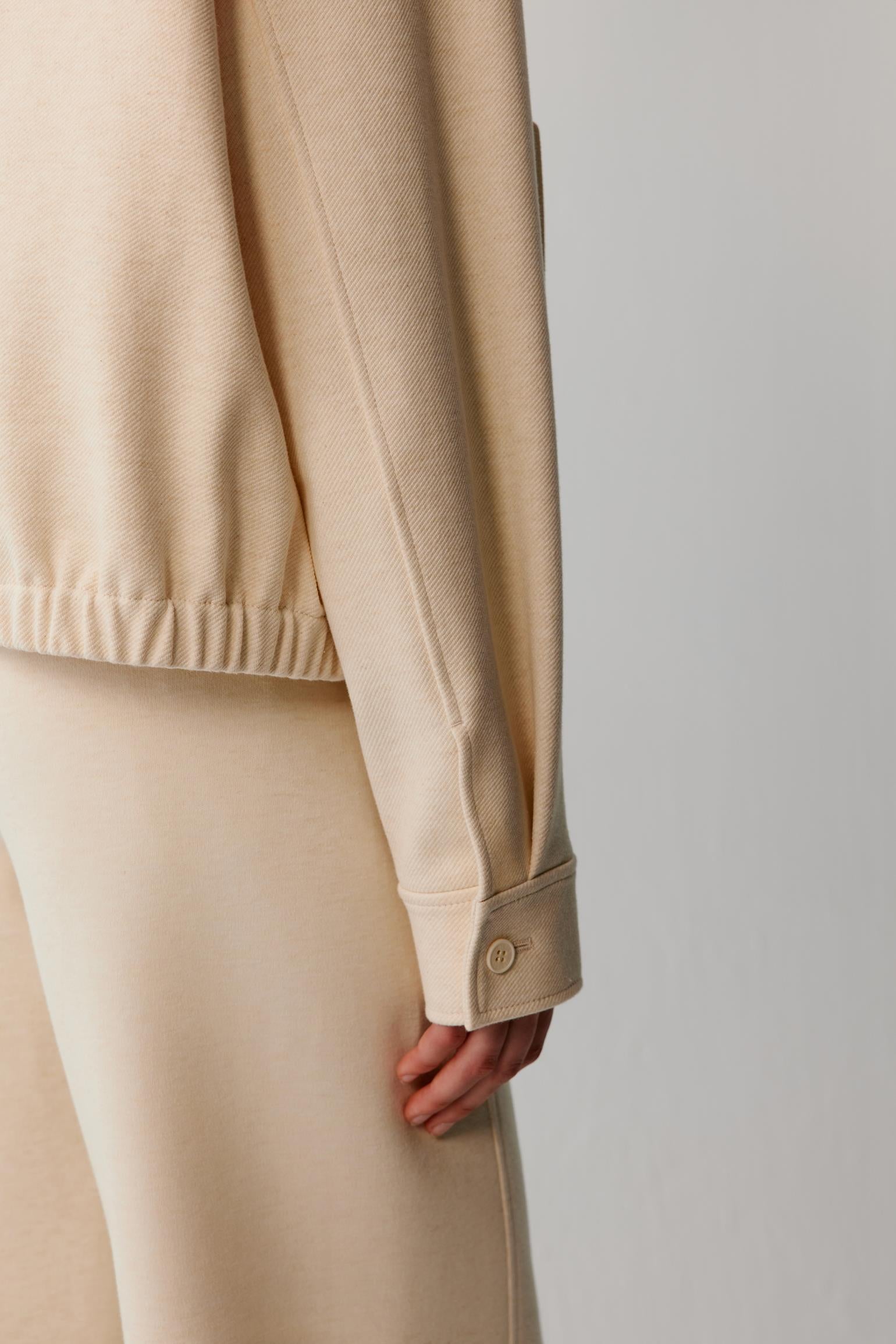 Close-up of the buttoned cuff, sleeve seam and elasticated hem of a cream jacket.