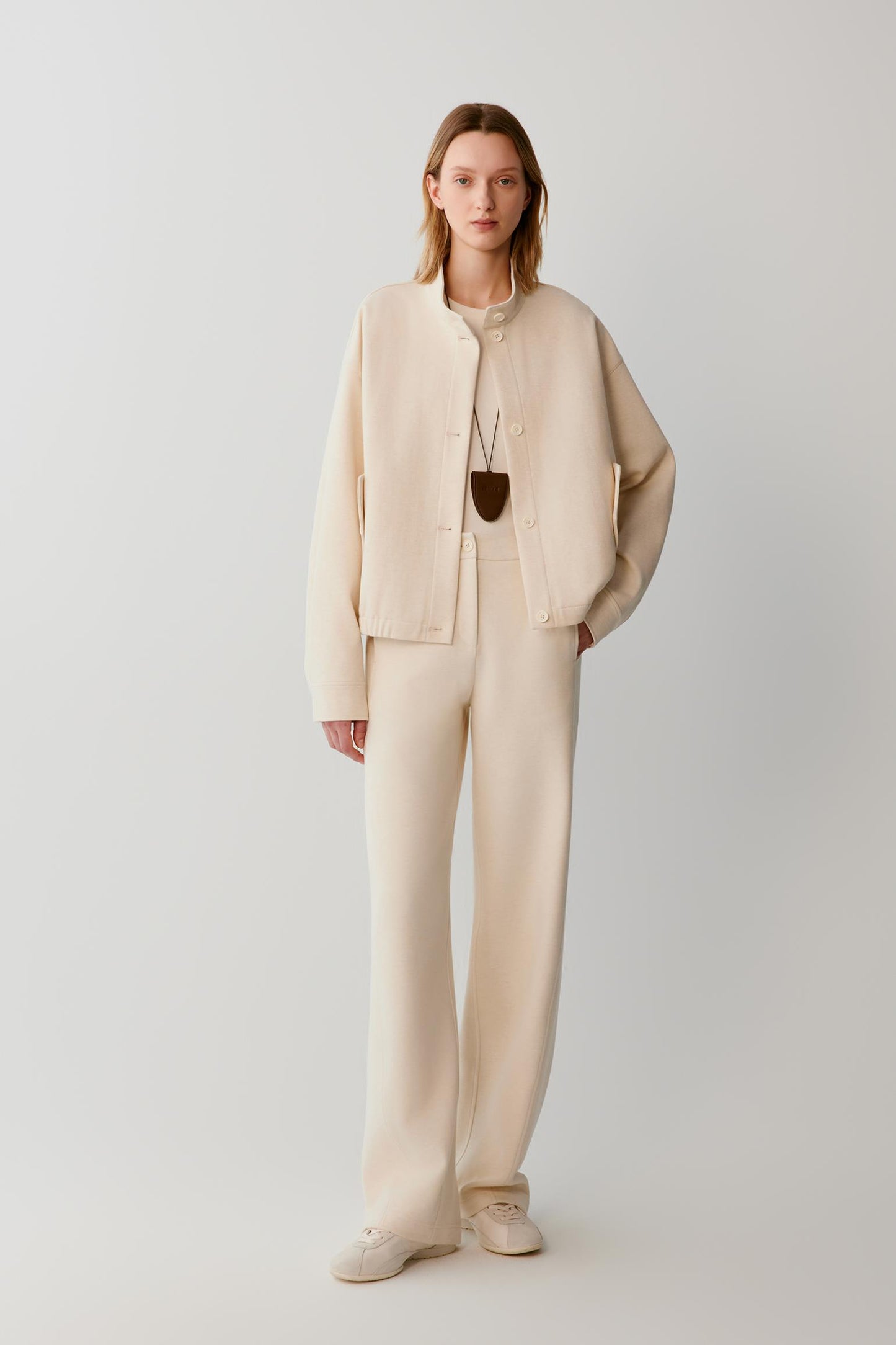 Woman wearing a cream textured jacket with matching wide-leg trousers and trainers.