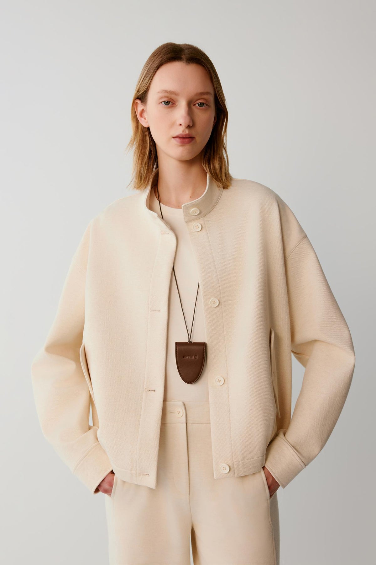 Woman wearing a cream textured button-up jacket with matching trousers.