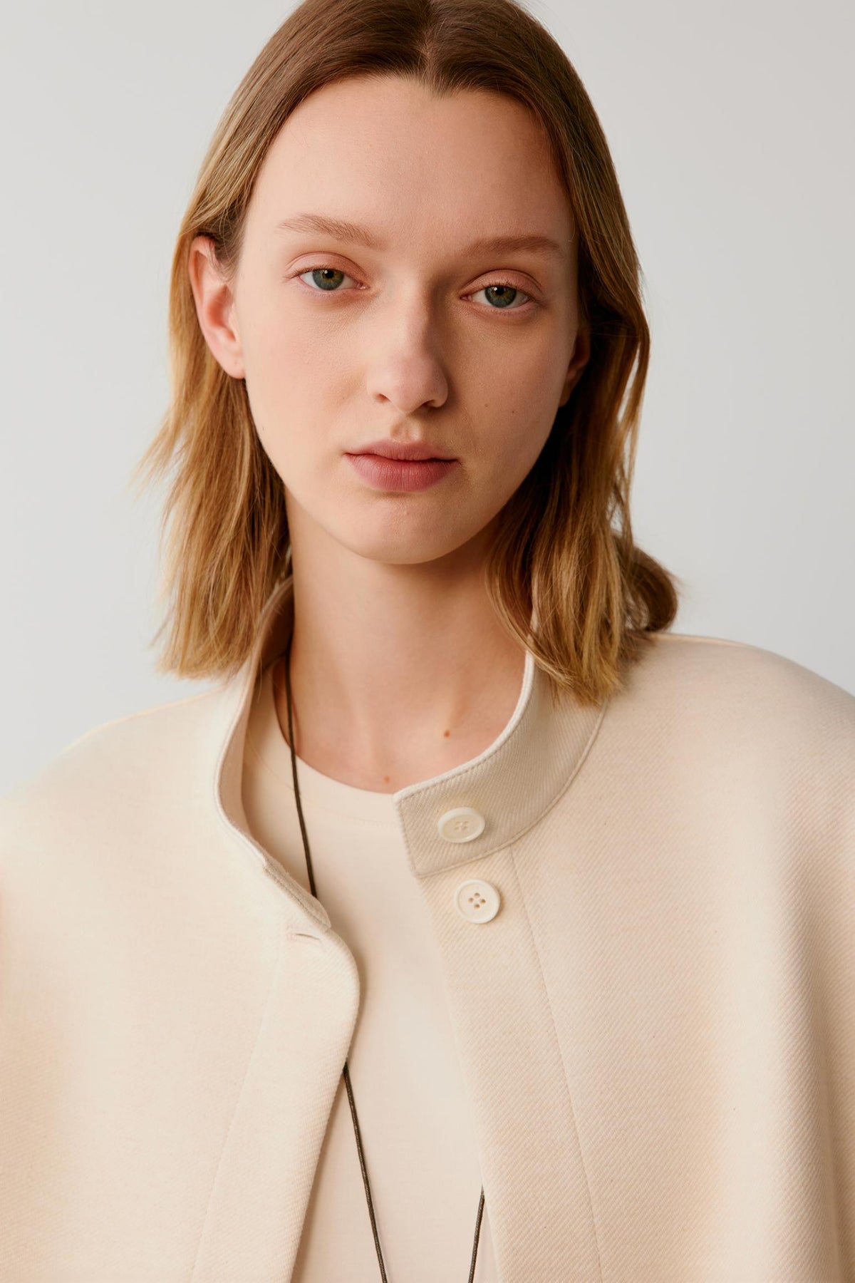 Close-up of a woman wearing a cream textured jacket with a round collar and buttons.