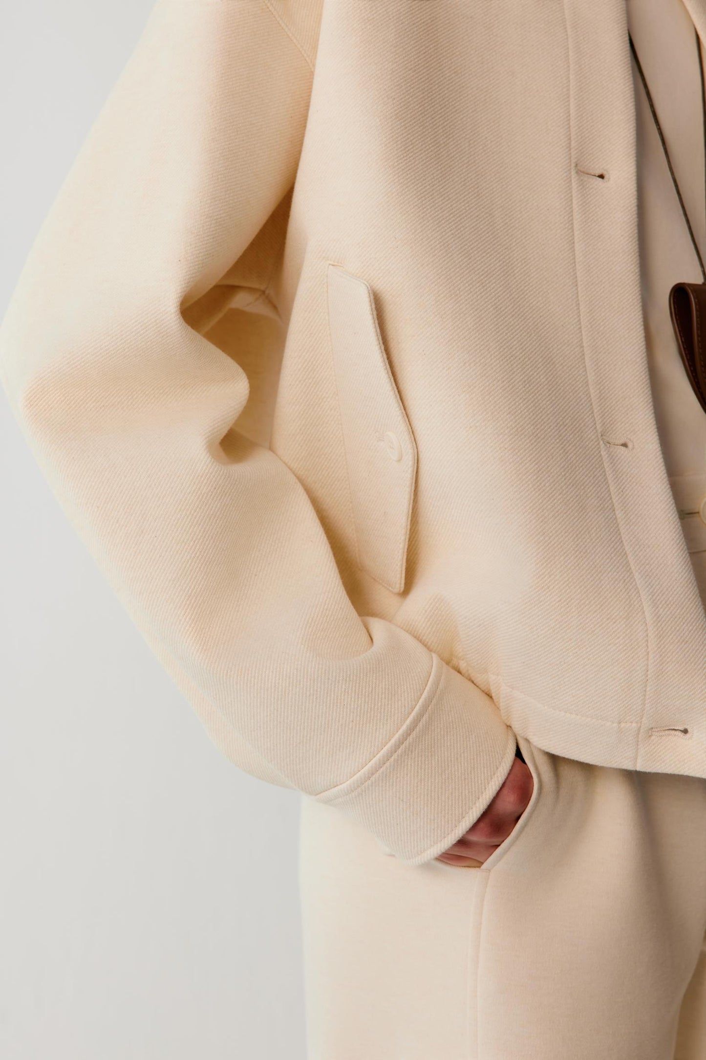 Close-up of the flap pocket, cuff and textured fabric of a cream jacket.
