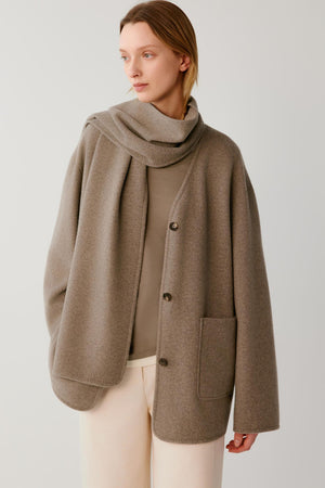 Woman wearing a taupe button-up jacket with a matching scarf and cream trousers.