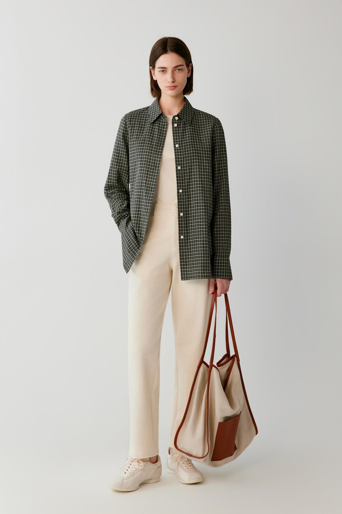 Woman wearing a black and cream checked shirt with cream trousers, carrying a two-tone tote bag.