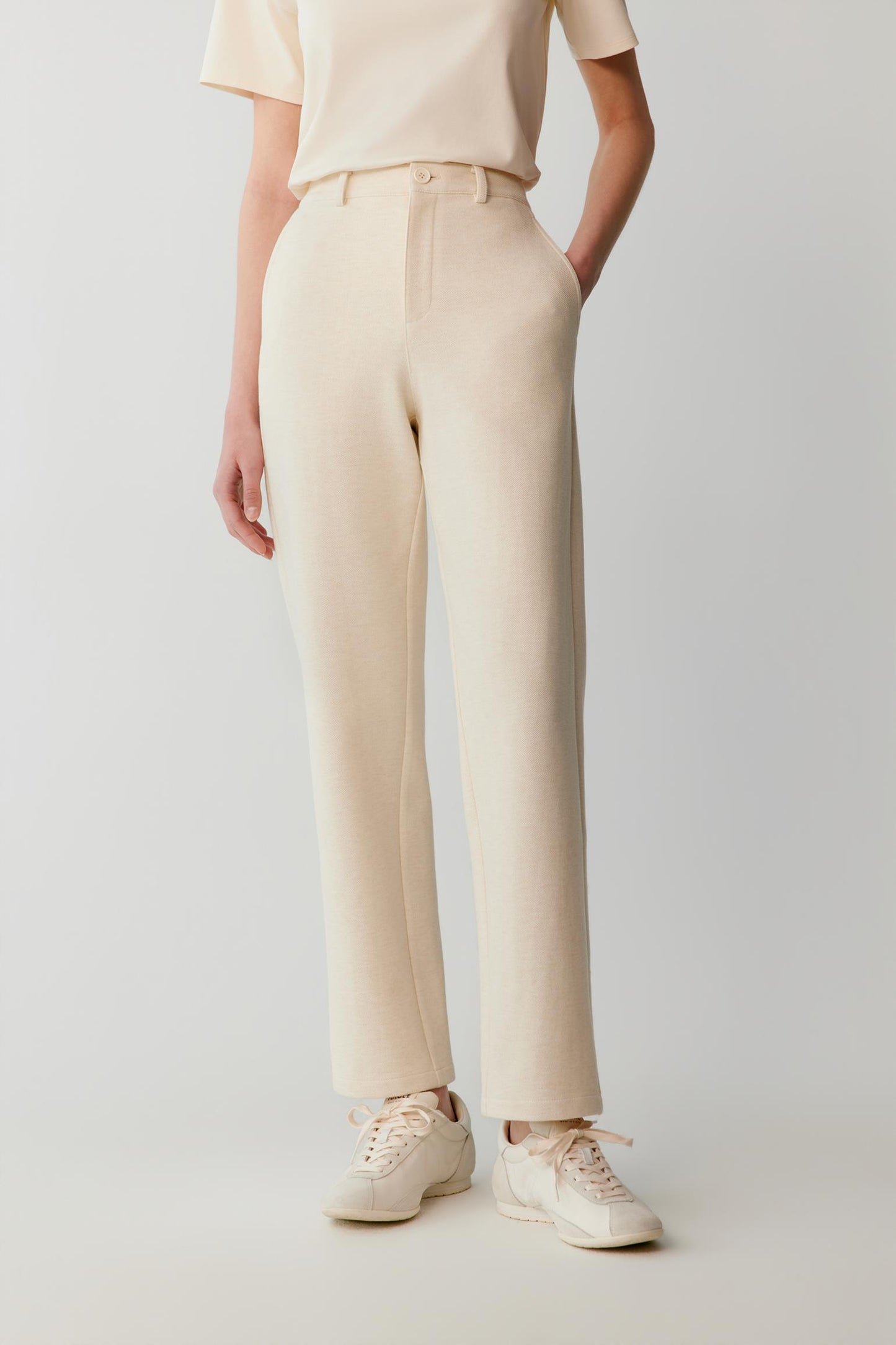 Woman wearing cream straight-leg tailored trousers with a matching top and white trainers.