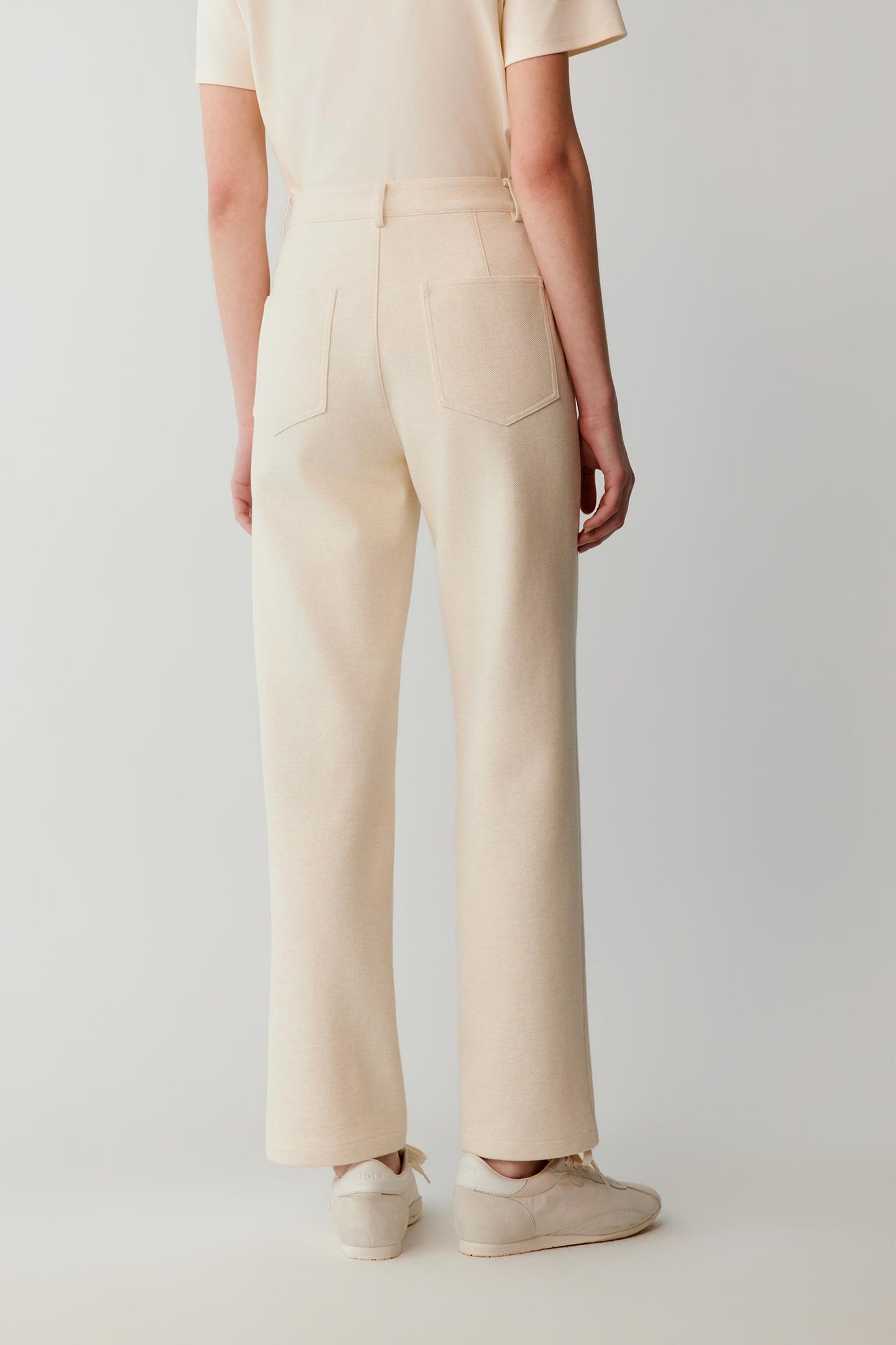 Back view of a woman wearing cream straight-leg trousers with patch pockets.