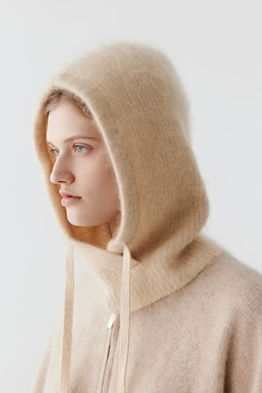 Side view of a woman wearing a beige knit hood with long ties on a light background