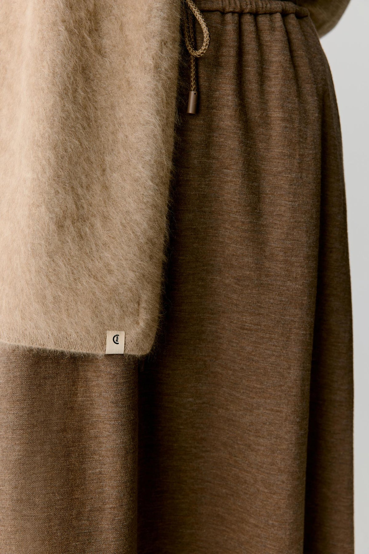 Close-up detail of the scarf hanging vertically, highlighting the smooth construction, soft folds and fluid movement of the cashmere fabric. The image emphasizes the subtle tonal depth and refined surface texture.