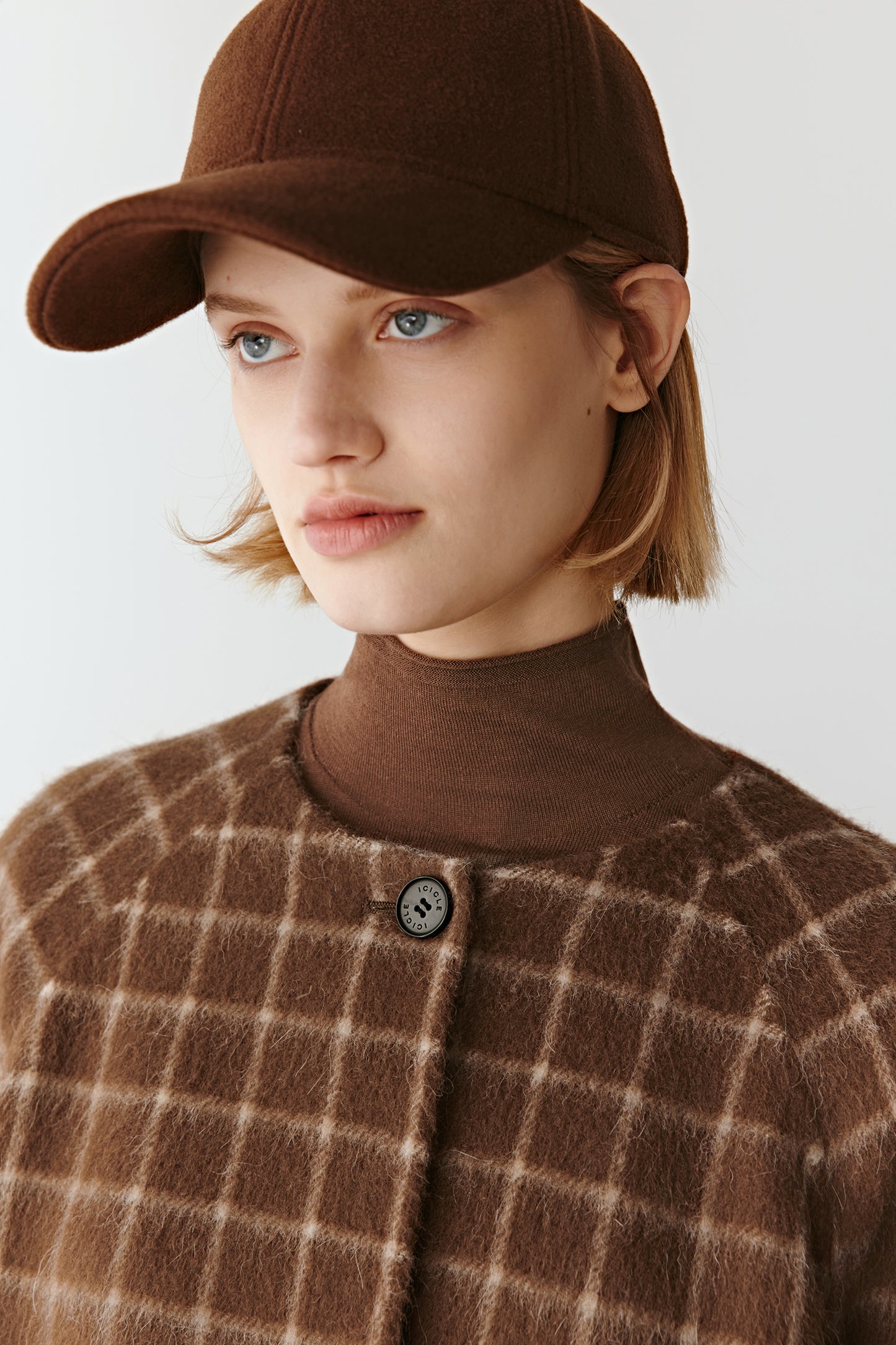 Close-up of the upper section of the short checked wool coat, focusing on the round neckline and brushed fabric.