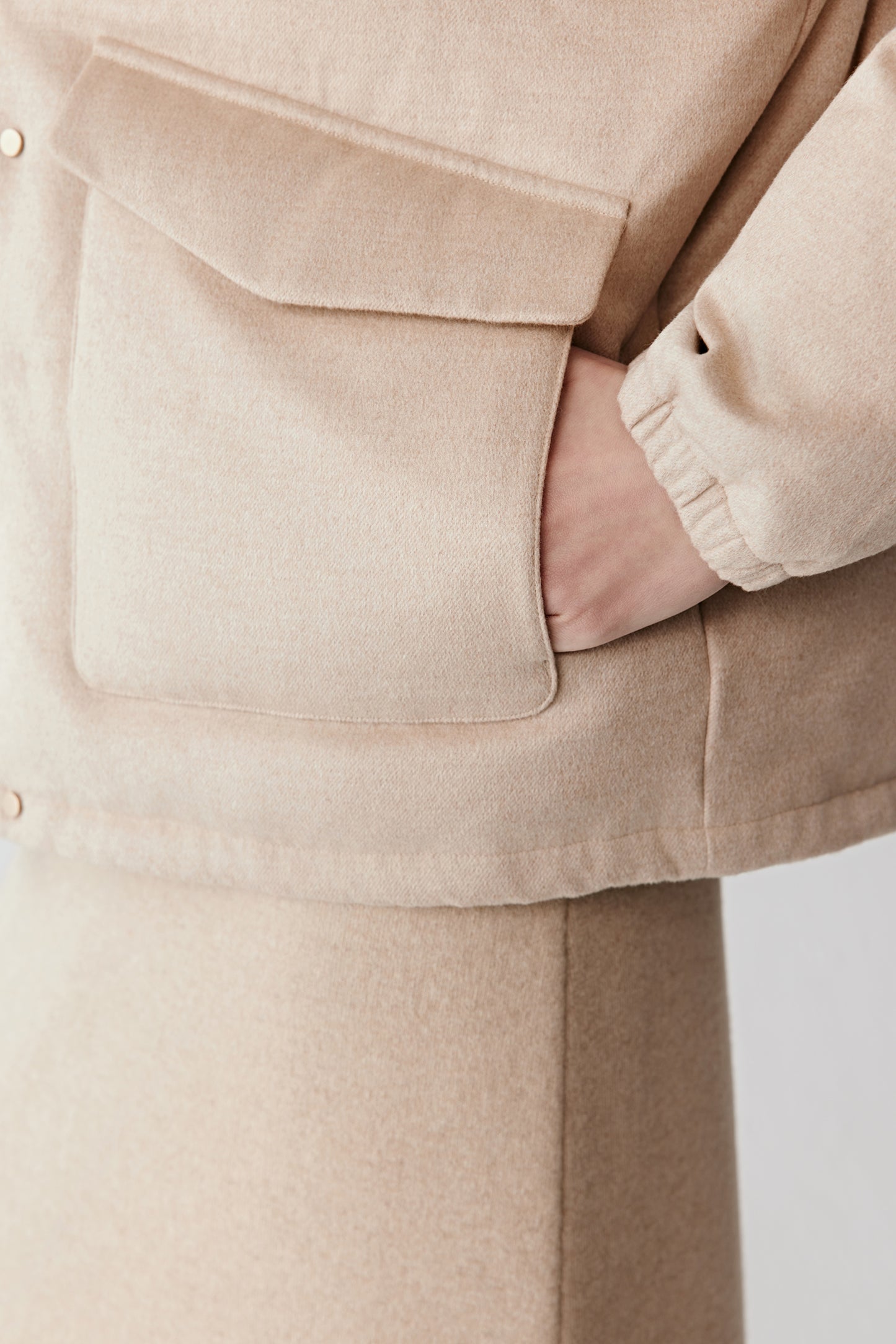 Detail close-up of the camel down coat’s adjustable hem with a discreet metal toggle and soft tweed fabric.