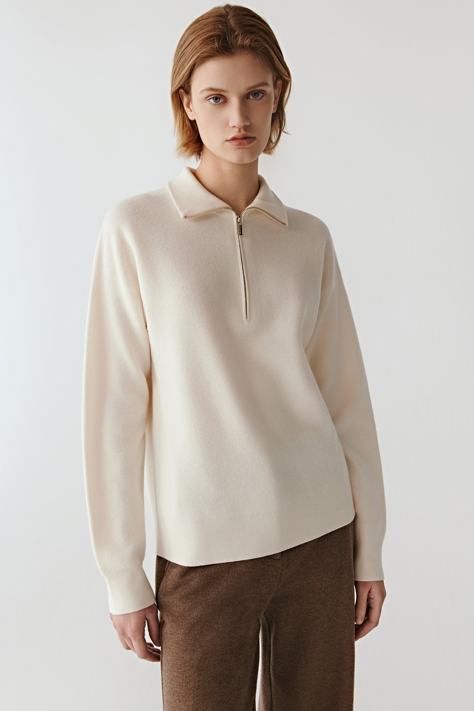Front view of a cream worsted wool pullover with a zipped stand collar and clean, minimalist lines.