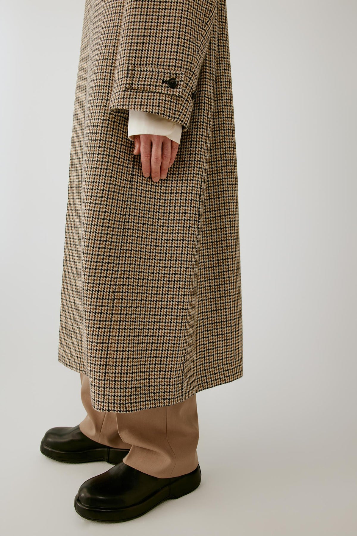 Close-up of the sleeve highlighting the adjustable cuff tab and structured houndstooth wool fabric.