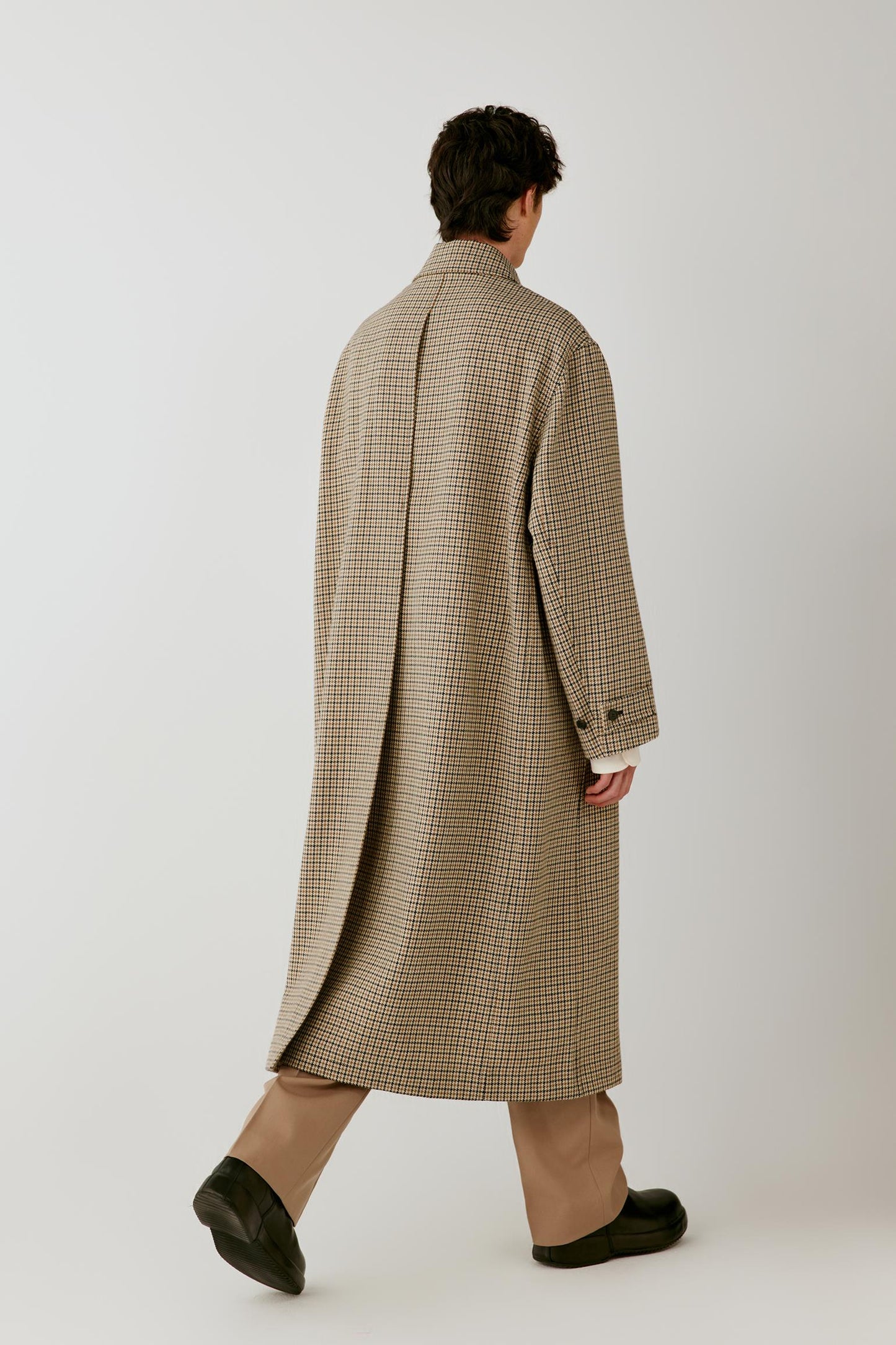 Back view showing the long silhouette, rear vent and clean construction of the houndstooth wool coat.