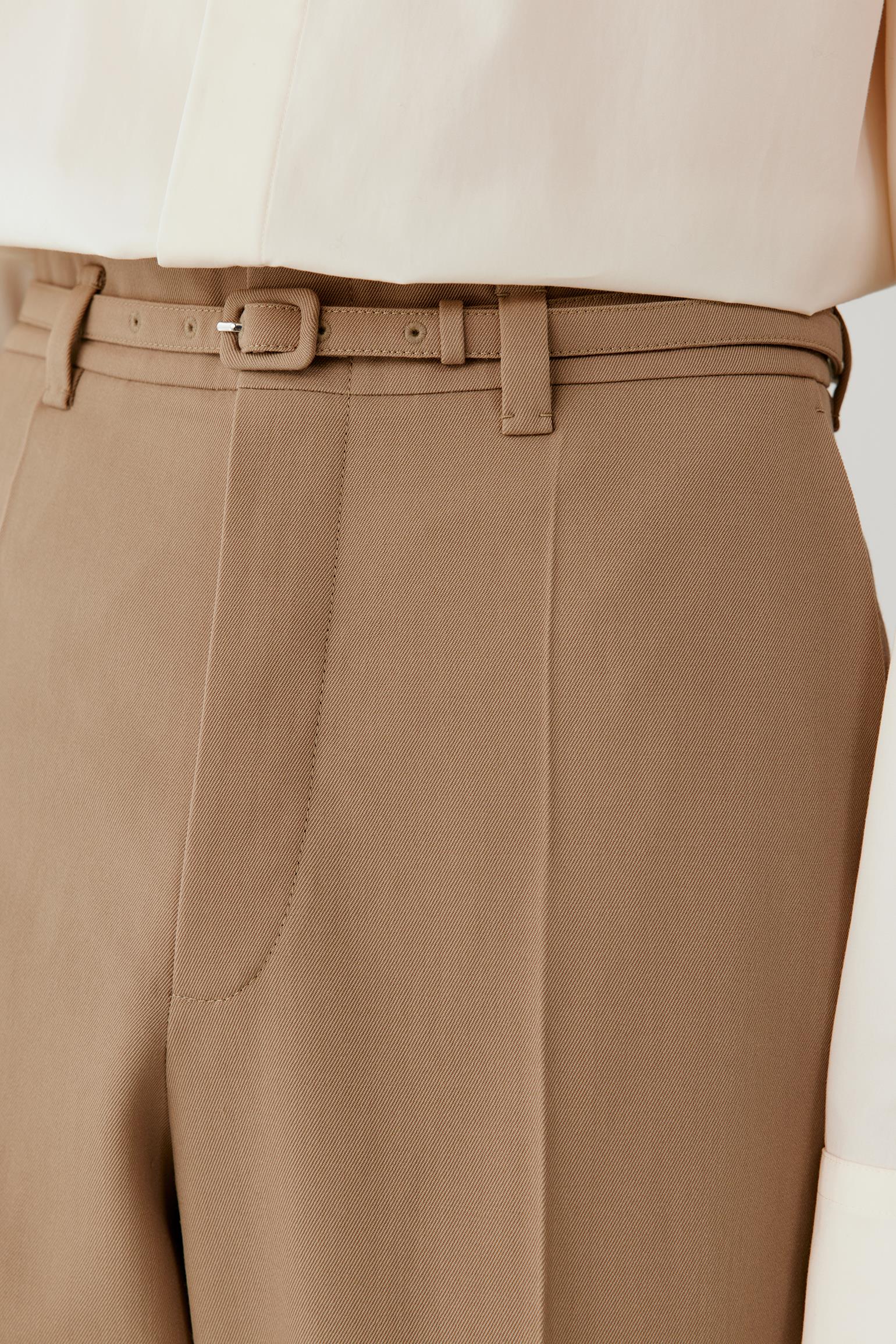 Close-up of the front waistband, showing the metal buckle belt loops and smooth, compact wool twill surface.