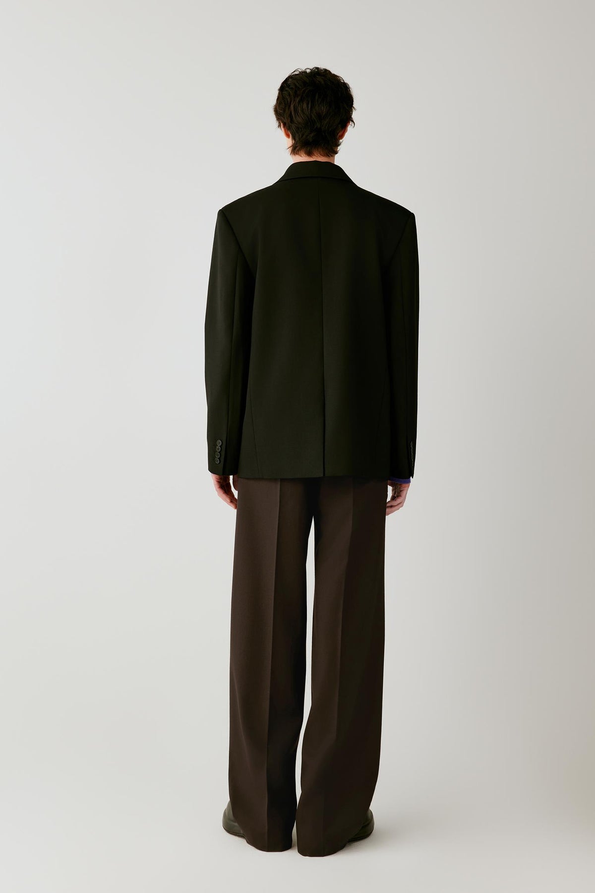 Back view showing the clean construction and straight silhouette of the black wool twill jacket.