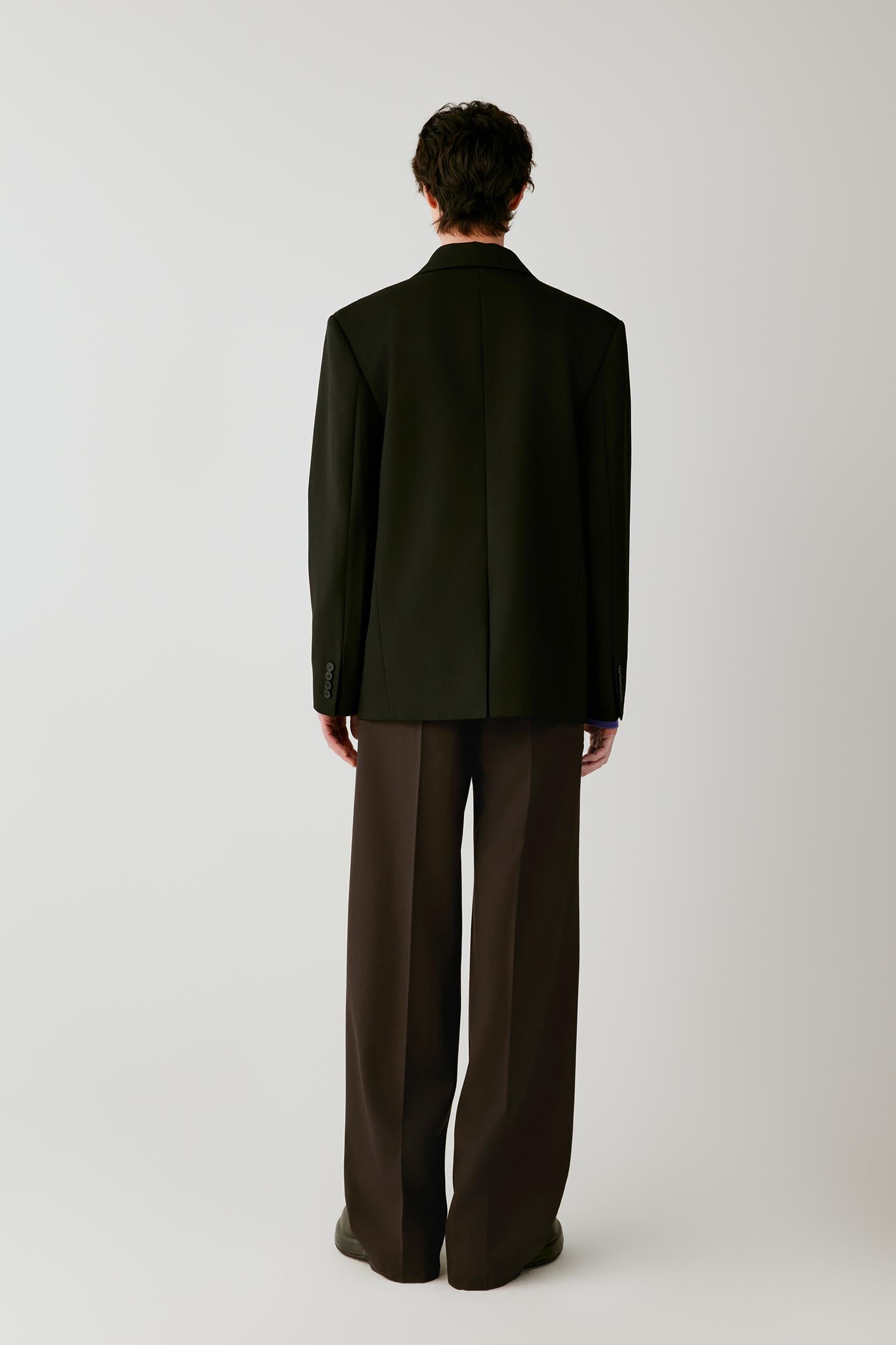 Back view showing the clean construction and straight silhouette of the black wool twill jacket.