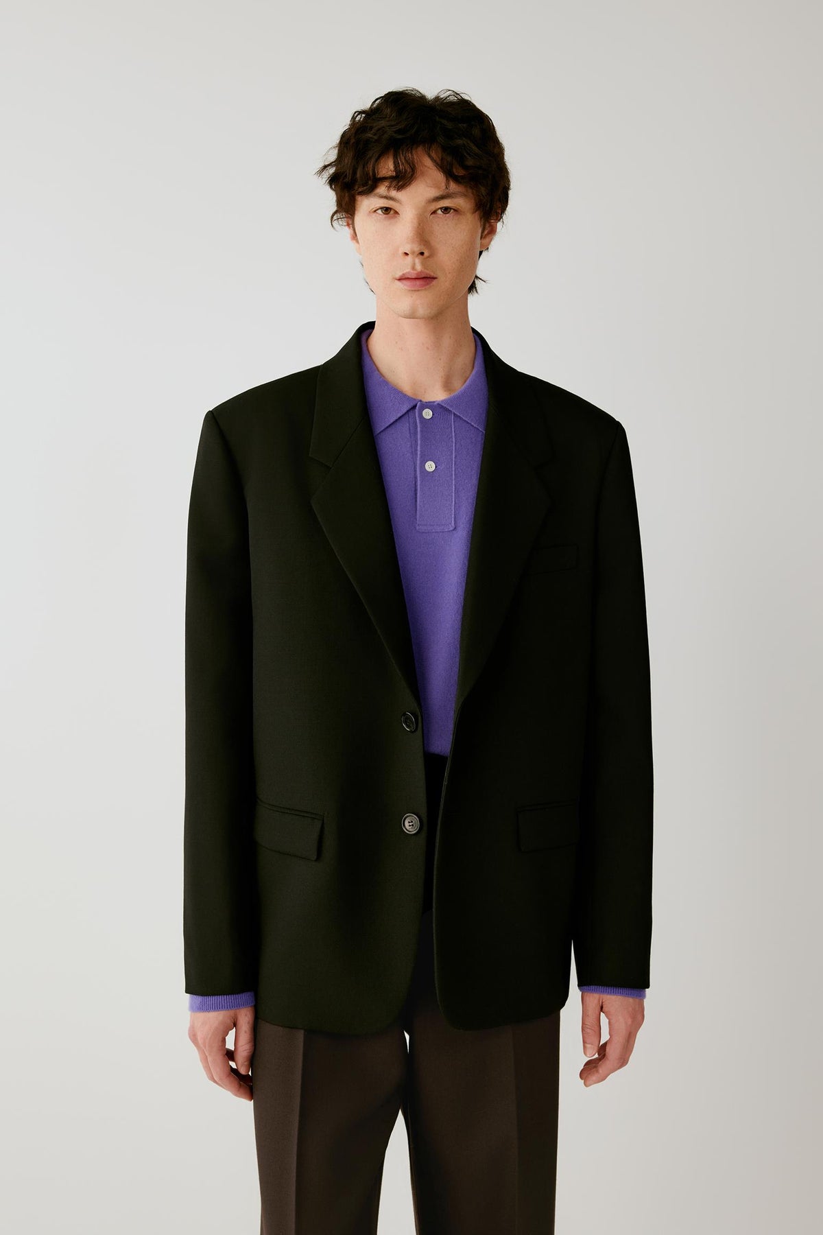 Front view of a man wearing a black wool twill jacket, highlighting the straight silhouette, notched lapels and two-button fastening.