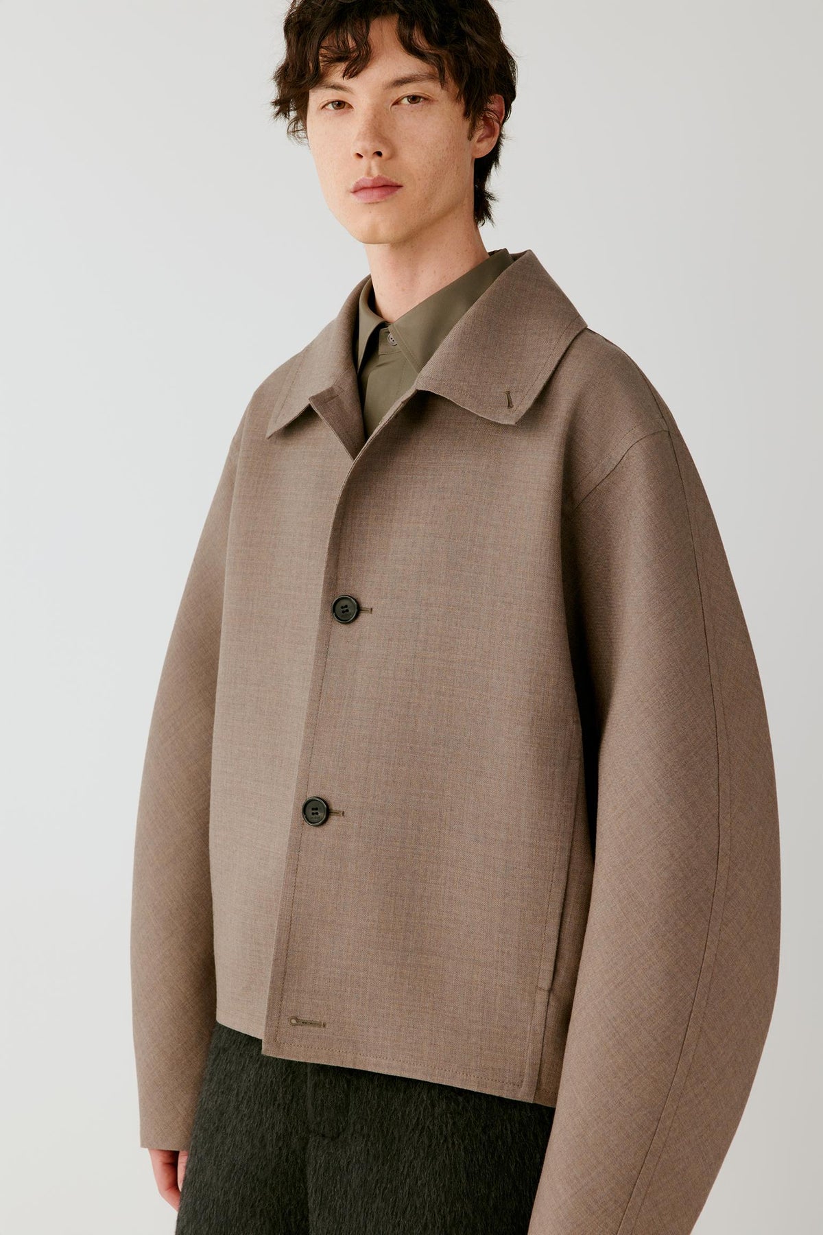 Front view of a man wearing a taupe melange wool and silk jacket, highlighting the cropped silhouette, pointed collar and concealed fastening.