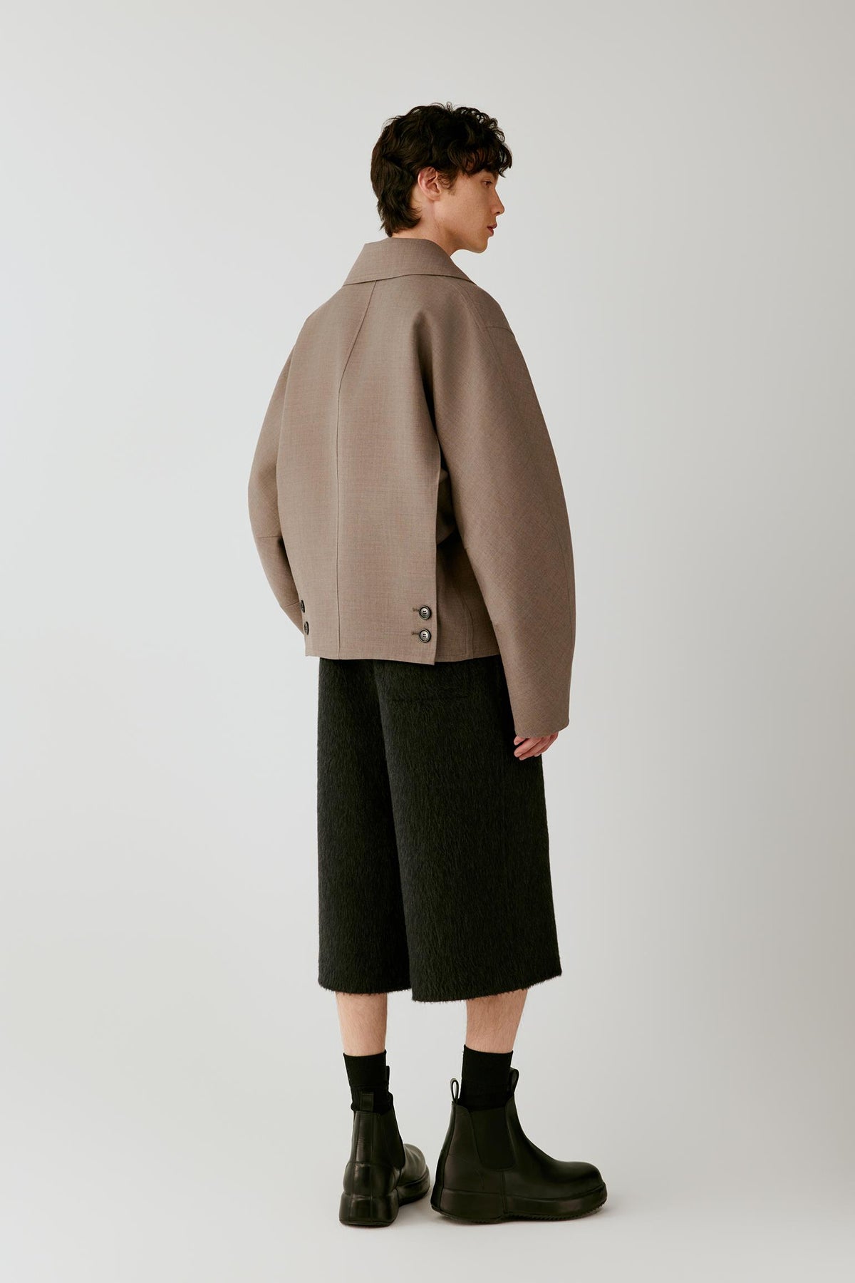Full-length side view highlighting the cropped cut, dropped shoulders and structured drape of the jacket.
