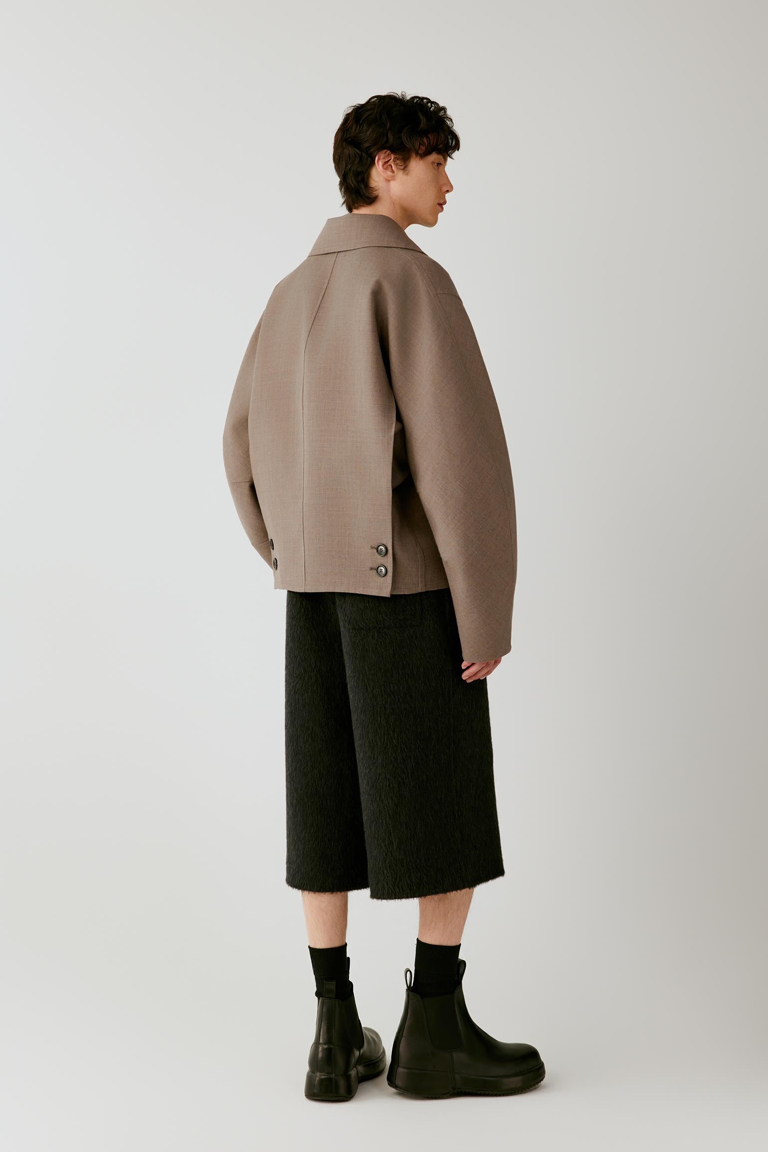 Full-length side view highlighting the cropped cut, dropped shoulders and structured drape of the jacket.
