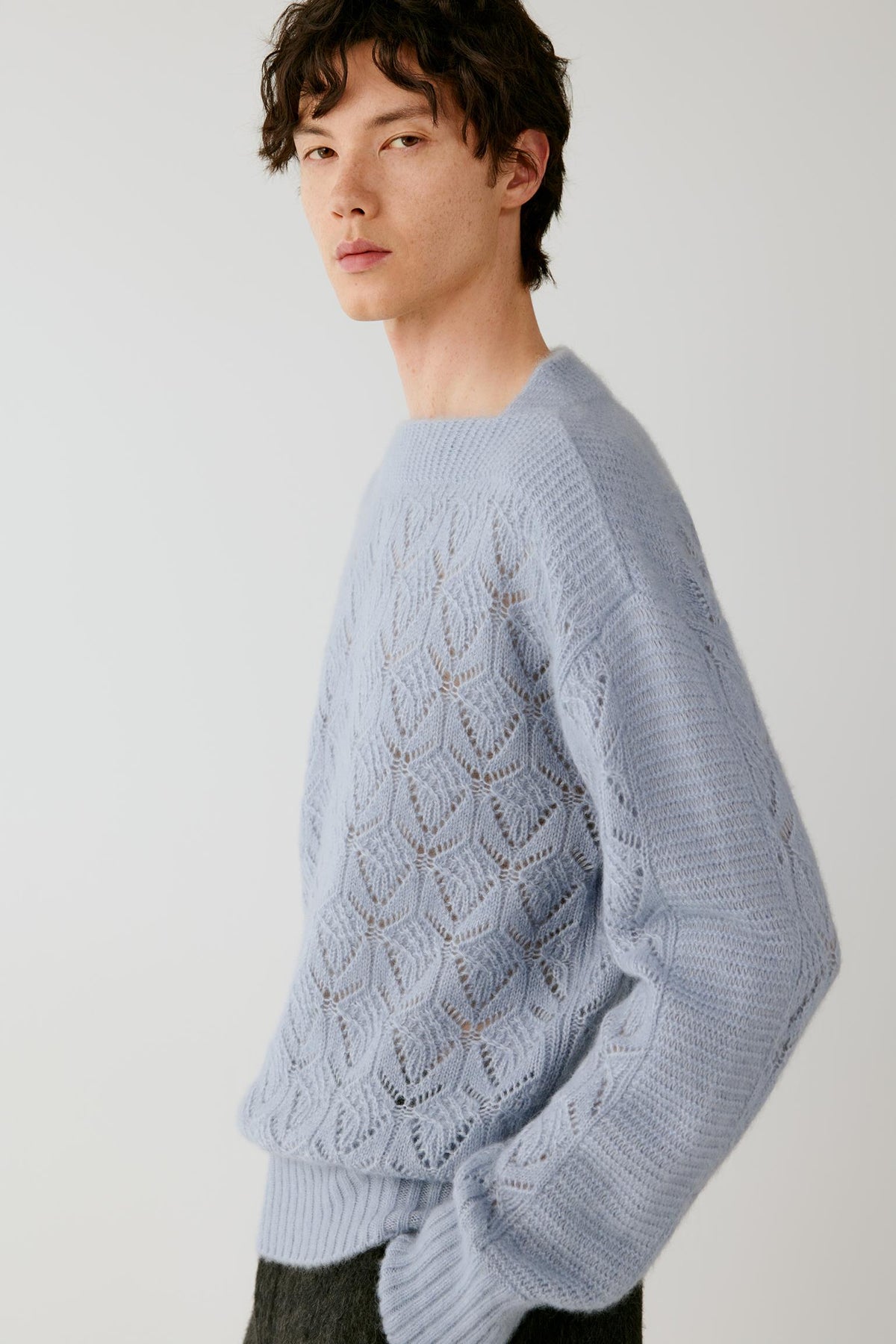 A man wearing a light blue textured knit sweater with a leaf-like openwork pattern, photographed against a plain light gray studio background.