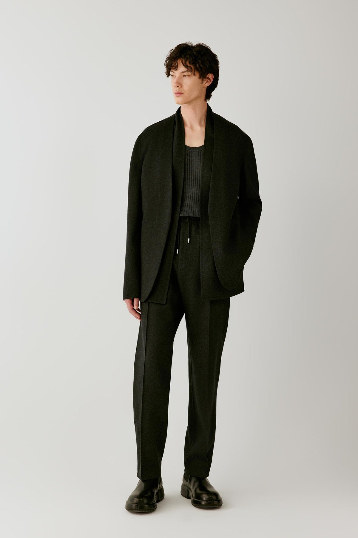 Full-length front view of a man wearing dark grey melange double-face wool trousers, highlighting the relaxed straight-leg silhouette and clean drape.