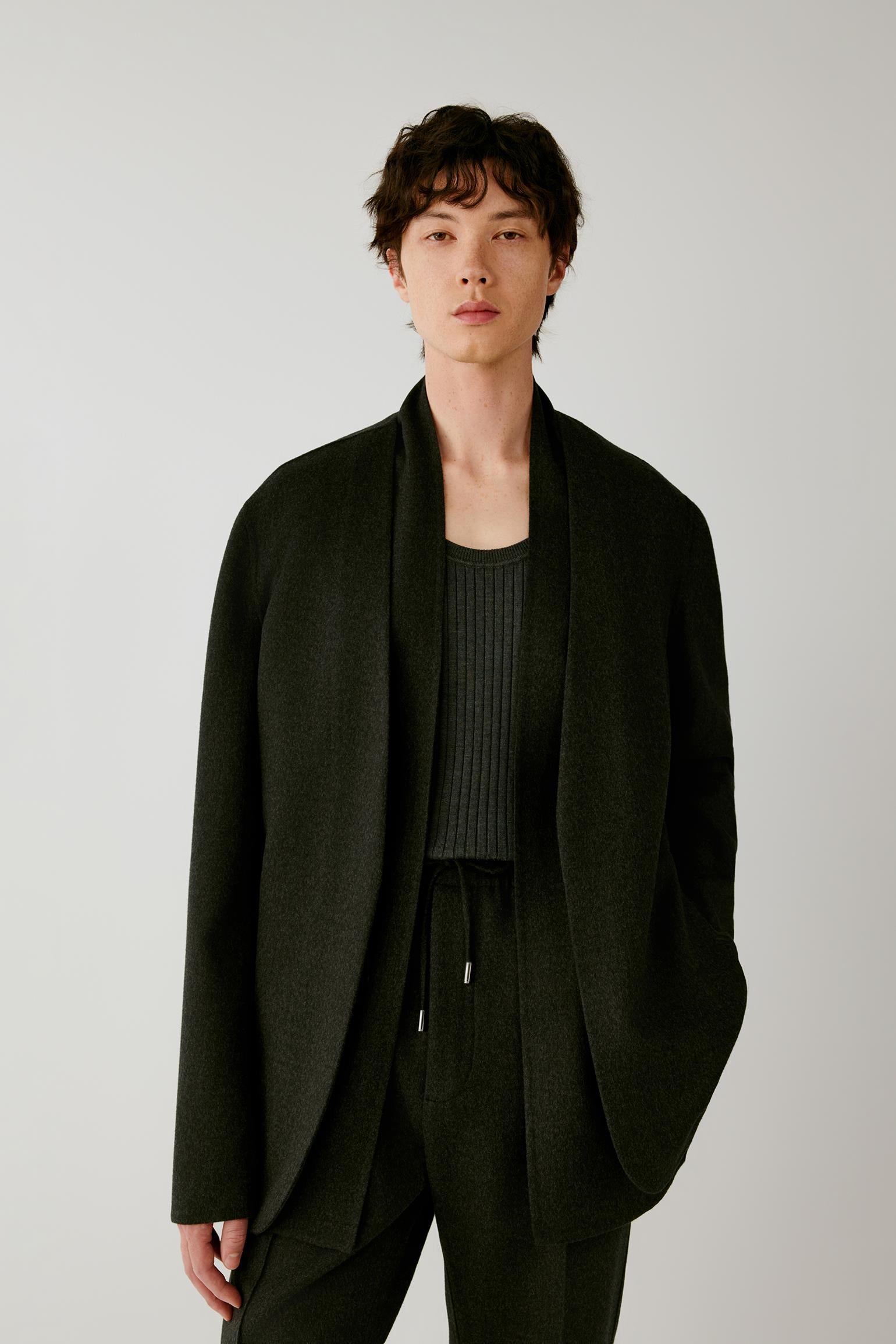 Front view of a man wearing a black double-face wool jacket, highlighting the relaxed silhouette, wide shawl collar and open front.