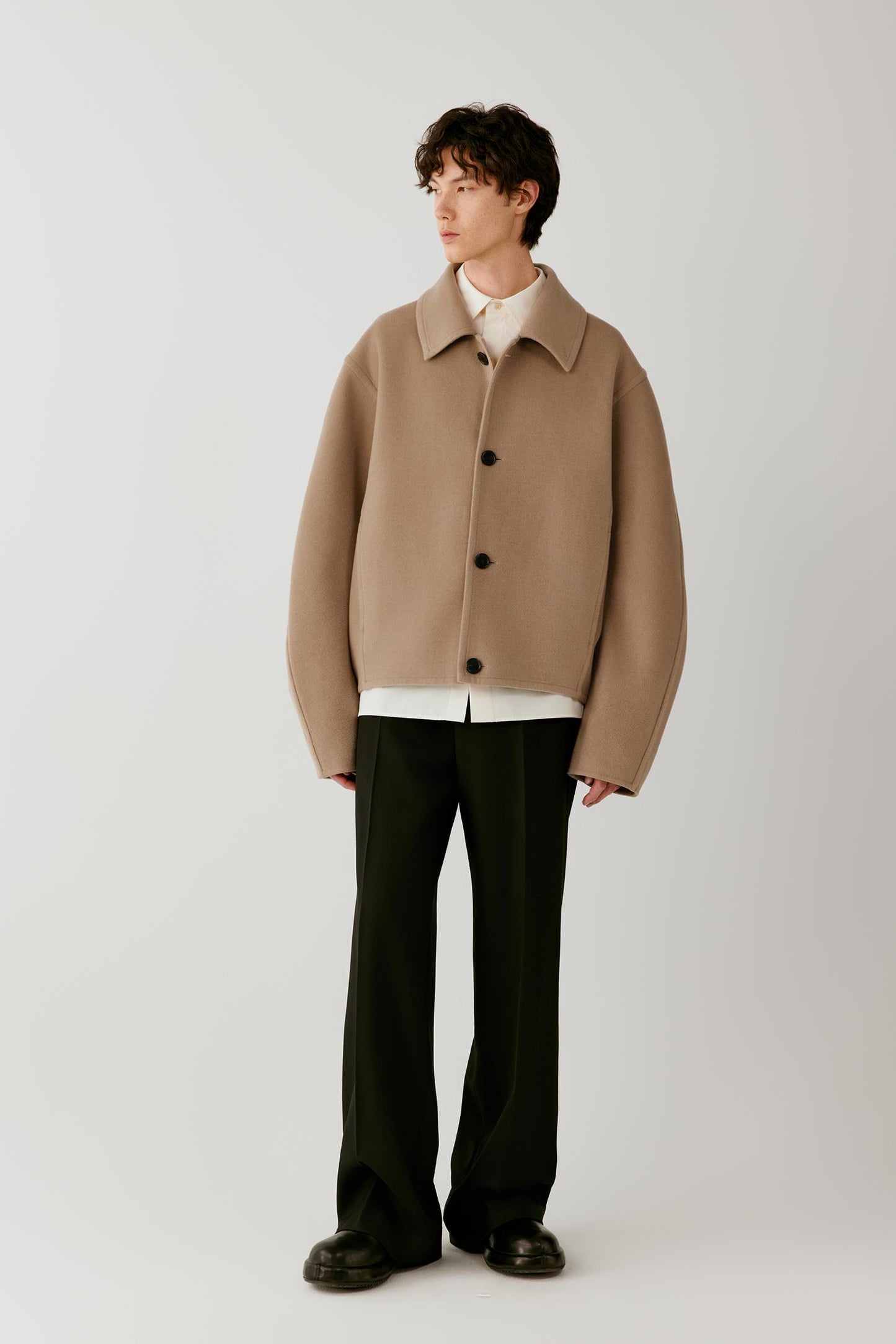 Full-length front view showing the short camel melange coat with black trousers, emphasizing the relaxed cut and concealed front fastening.