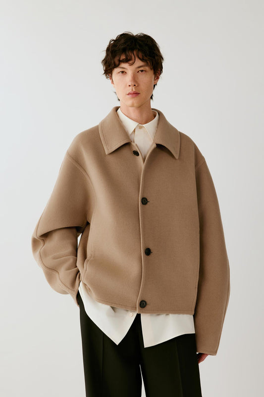 Three-quarter front view of a man wearing a camel melange double-face wool coat, highlighting the relaxed silhouette, pointed collar and clean construction.