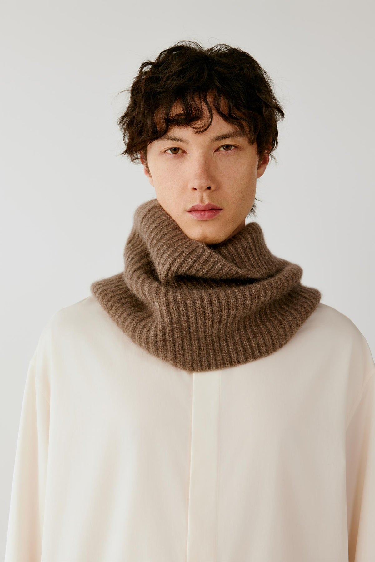 Close-up of a man wearing a brown ribbed knitted snood over a cream top.