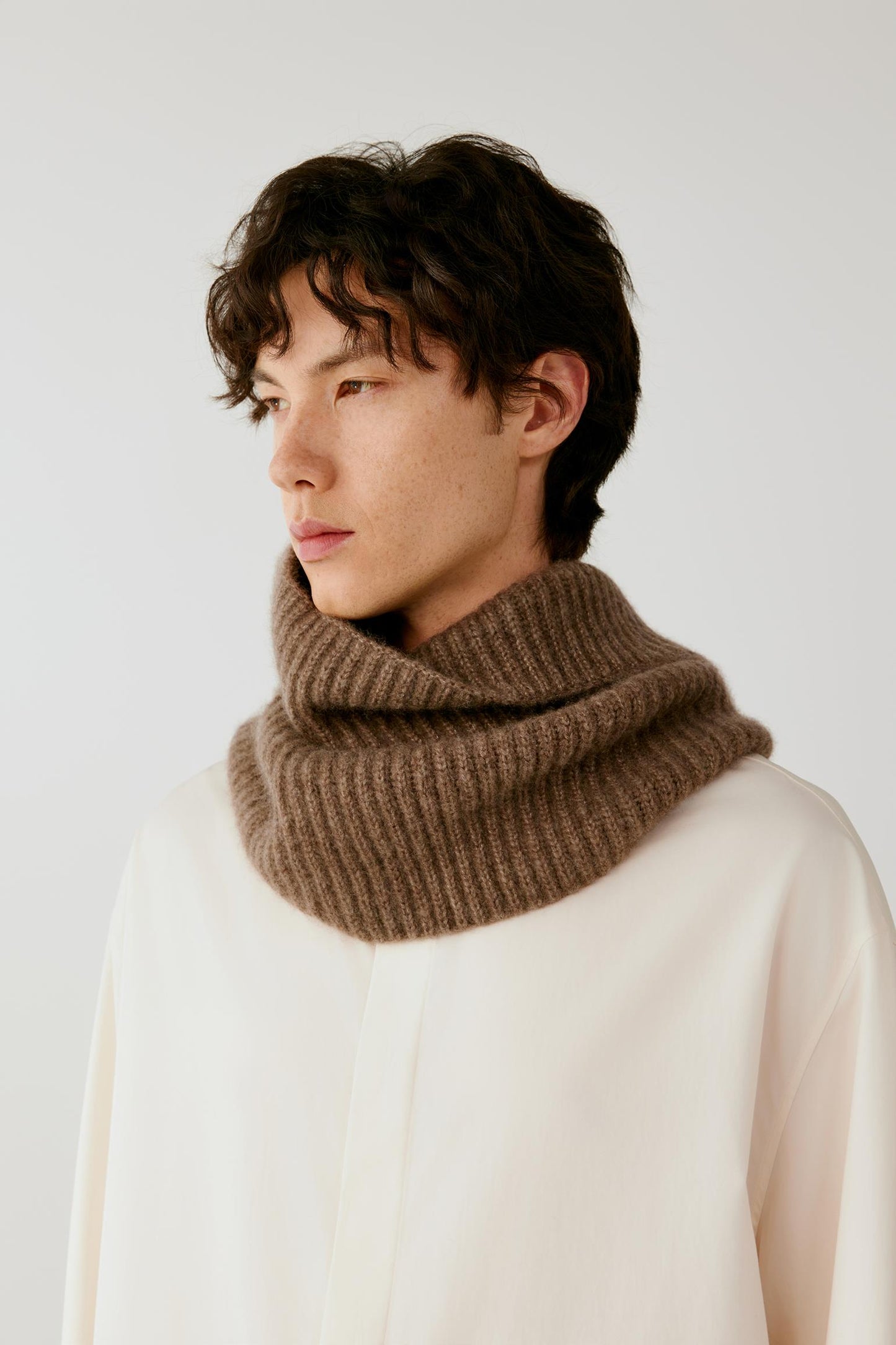 Close-up of a man wearing a brown ribbed knitted snood over a cream top.