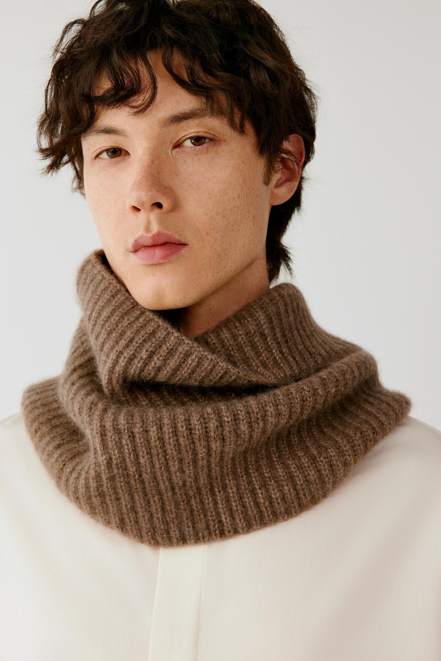 Close-up of a man wearing a brown ribbed knitted snood over a cream top.