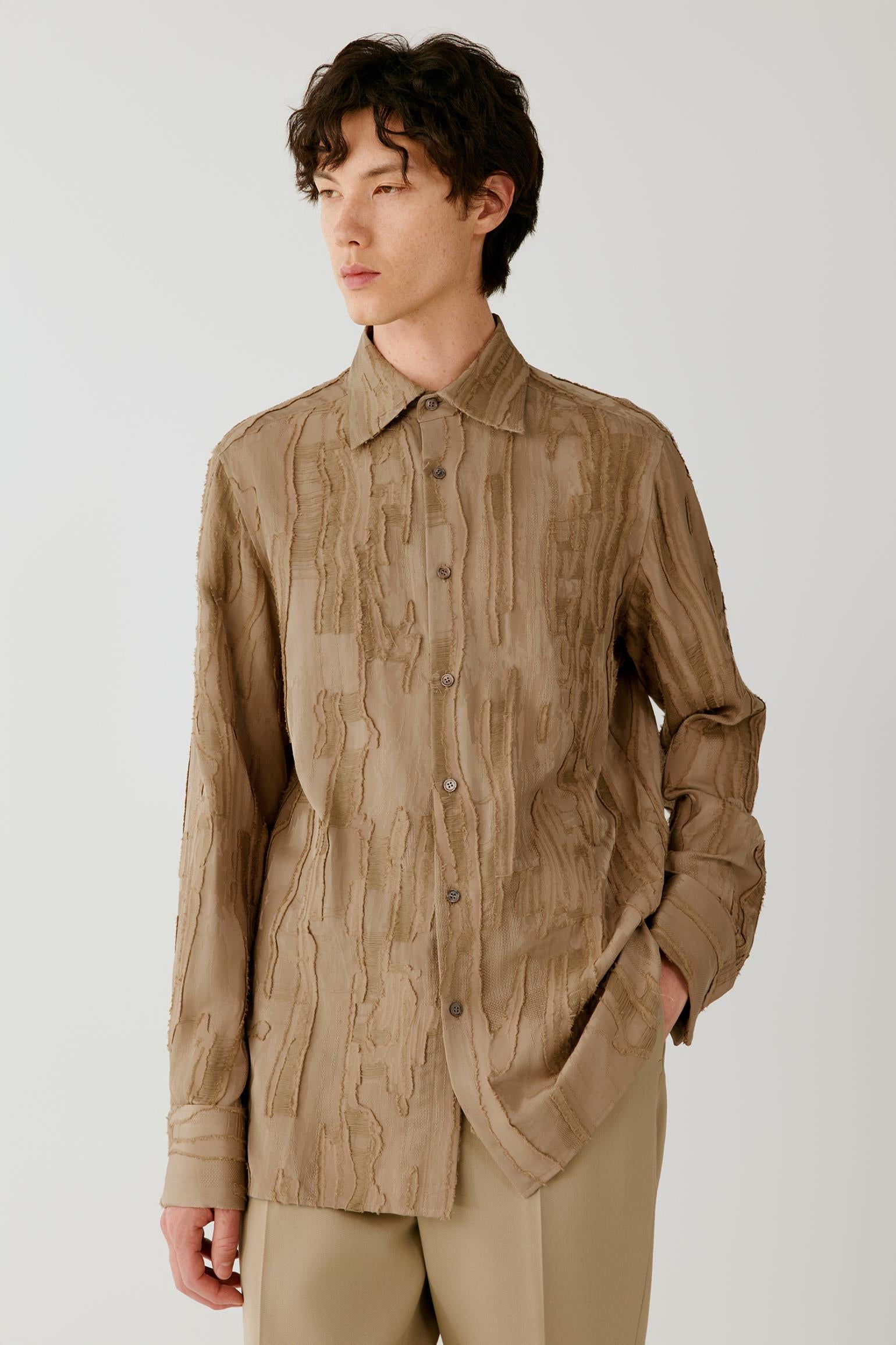 Three-quarter front view of a man wearing a camel jacquard shirt, highlighting the relaxed silhouette, pointed collar and textured wood-grain pattern.