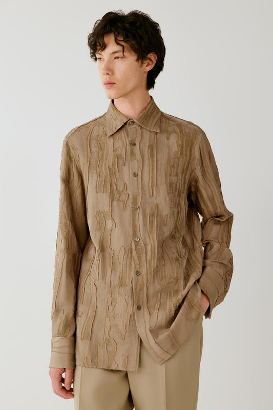 Three-quarter front view of a man wearing a camel jacquard shirt, highlighting the relaxed silhouette, pointed collar and textured wood-grain pattern.